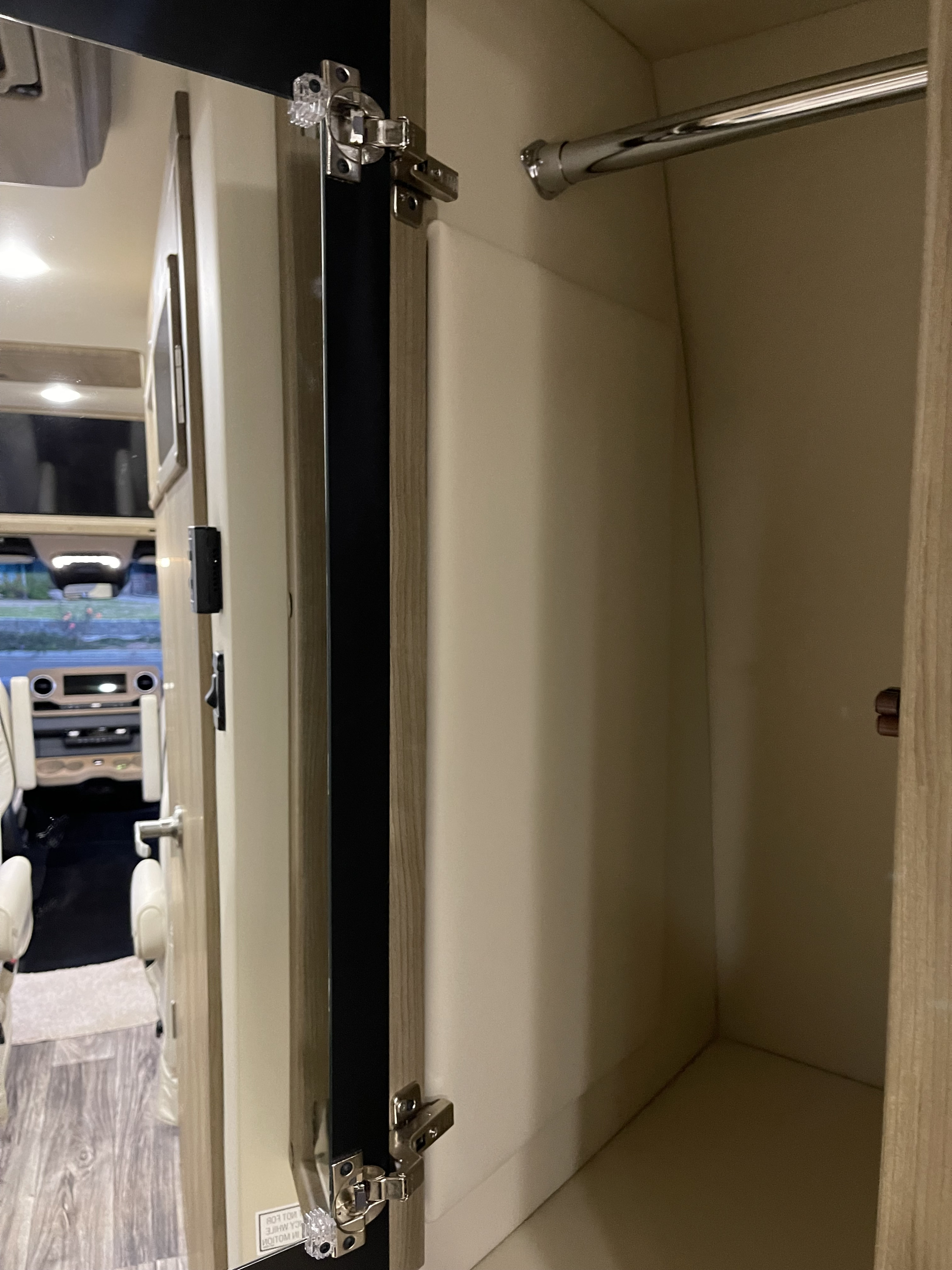 Inside an RV rental: a compact closet with a chrome hanging bar, offering storage. View into the vehicle's front cabin.. Midwest Automotive Designs Midwest Automotive Designs Class B 2022