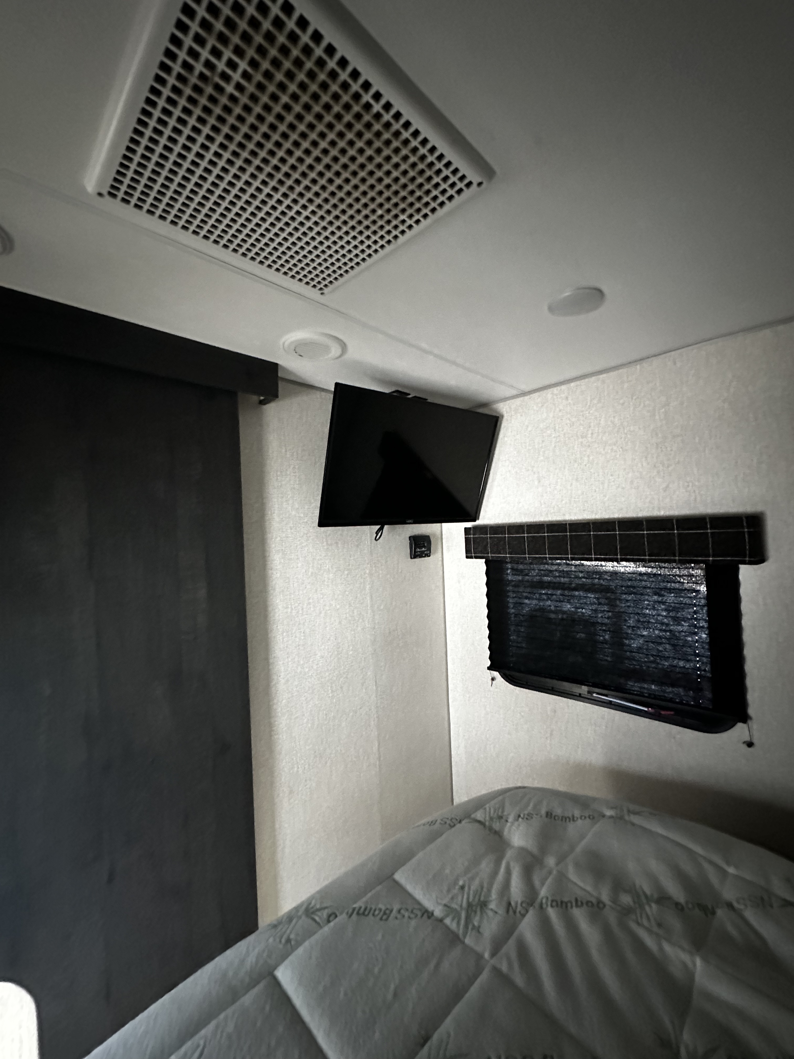 Inside an rv rental bedroom: mounted TV, AC vent, window with blind, and a comfy bed with an NS Bamboo mattress pad.. K-Z Manufacturing Sportsmen 2022