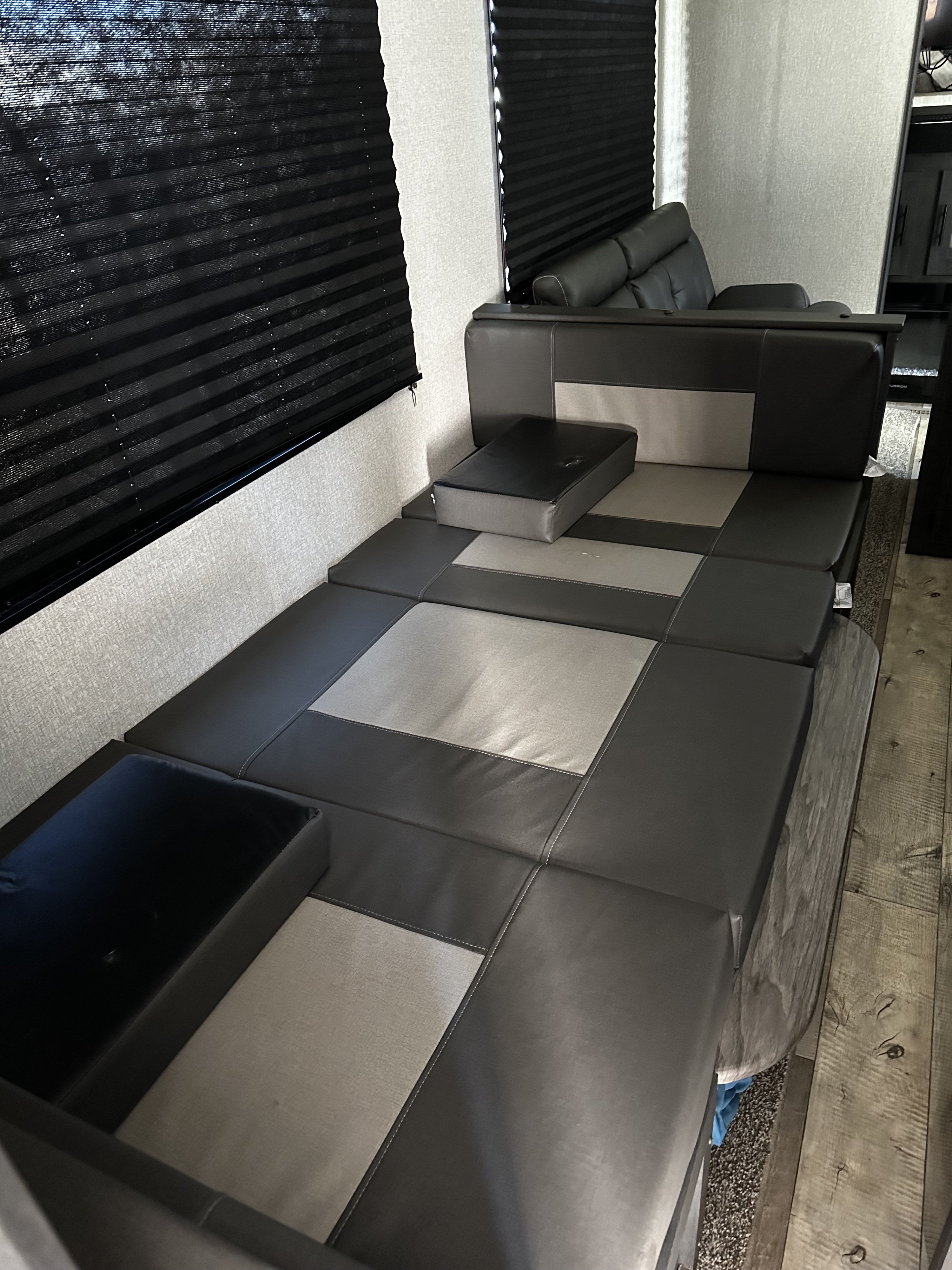 This RV rental's convertible dinette lounge, shown as a bed, with stylish dark and light gray cushions and blinds.. K-Z Manufacturing Sportsmen 2022