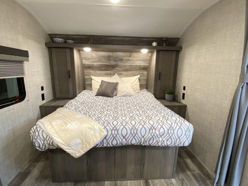Comfortable RV rental bedroom featuring a queen bed, wooden headboard, and practical built-in storage. Ready for travel!. Grand River 25BH 2024