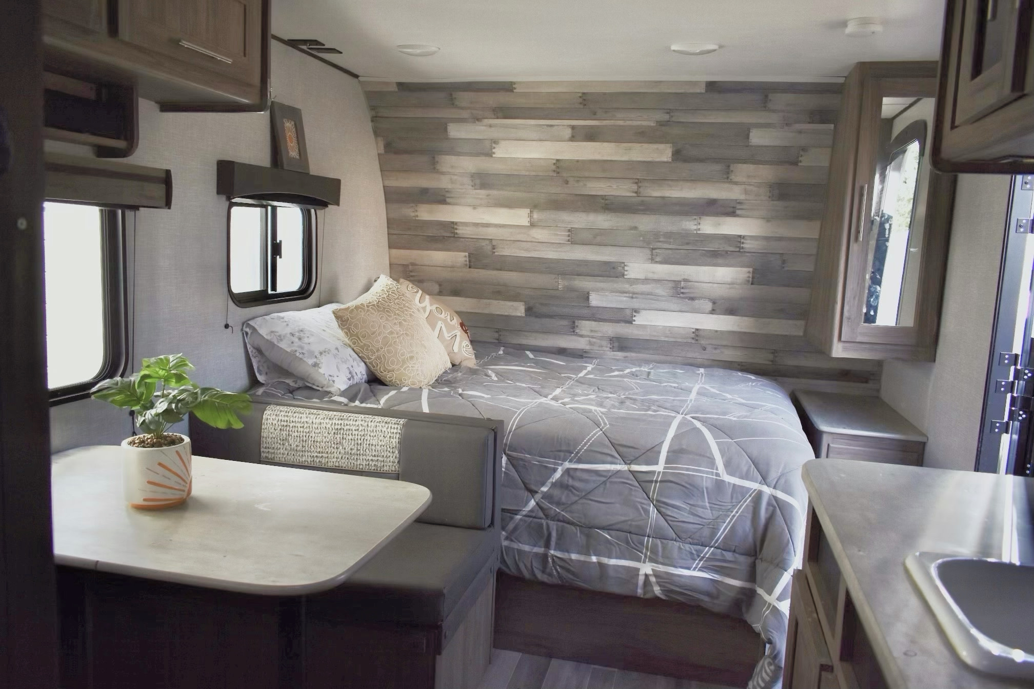 Inside an **RV rental**: view of bedroom with accent wall, dinette with plant, and part of kitchen sink. Compact, modern travel living.. Crossroads RV Zinger Lite 2022