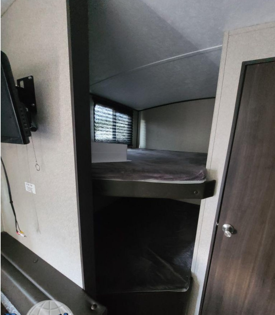 RV rental interior: bunk beds with mattresses & window blinds. TV mounted on left wall.. Keystone RV Springdale 2018