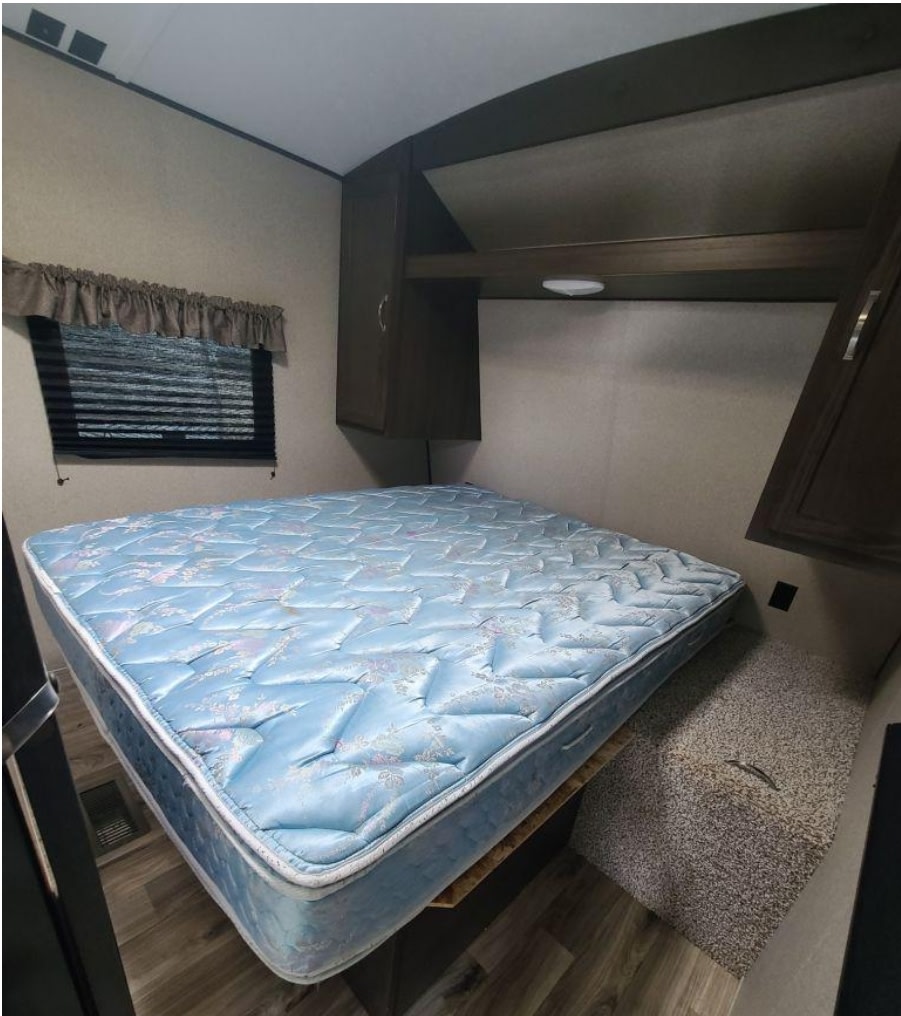 RV rental bedroom showcasing a comfortable mattress, overhead cabinets, and window with blinds.. Keystone RV Springdale 2018