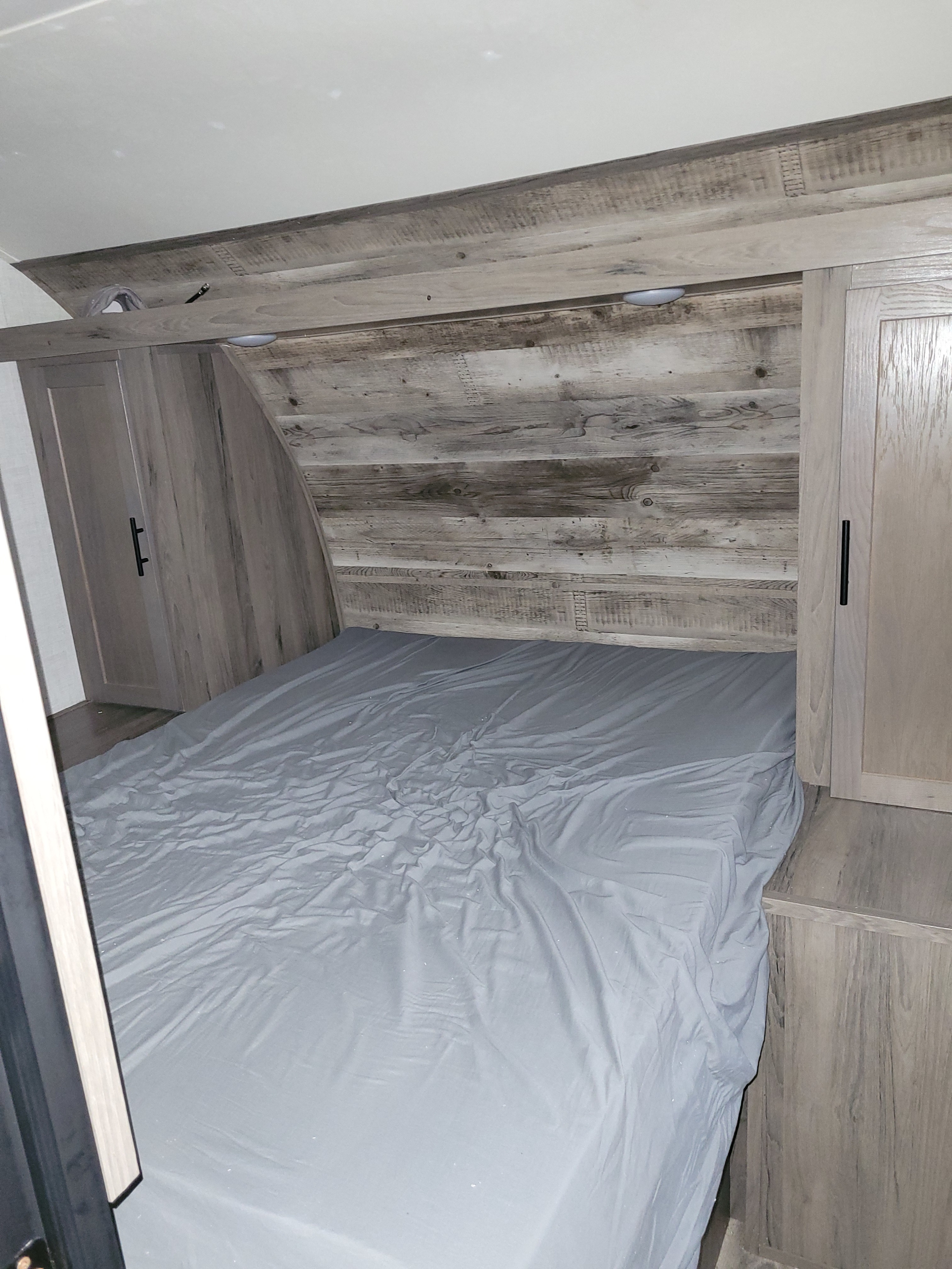 Cozy RV rental bedroom features a compact bed with grey sheets, wood-paneled walls, and built-in overhead storage.. Gulf Stream Ameri-Lite 2021