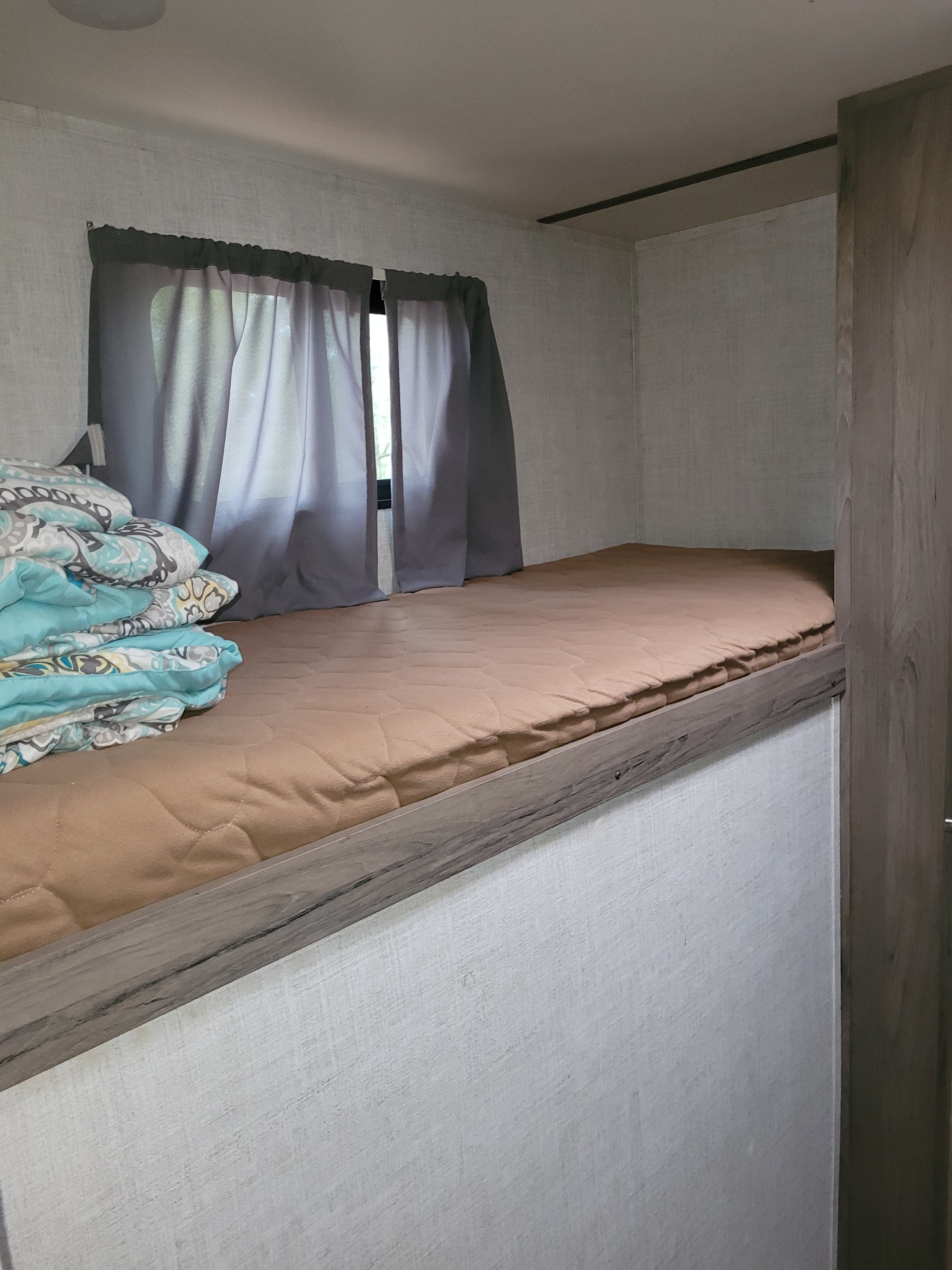 RV rental bunk bed interior with a brown mattress, window, and stacked blue/patterned blankets for cozy sleeping.. Gulf Stream Ameri-Lite 2021