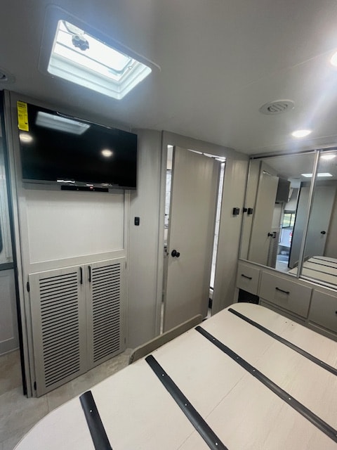 Compact RV rental bedroom featuring a TV, skylight, and mirrored storage, offering a cozy, modern retreat.. Coachmen FREELANDER 2025