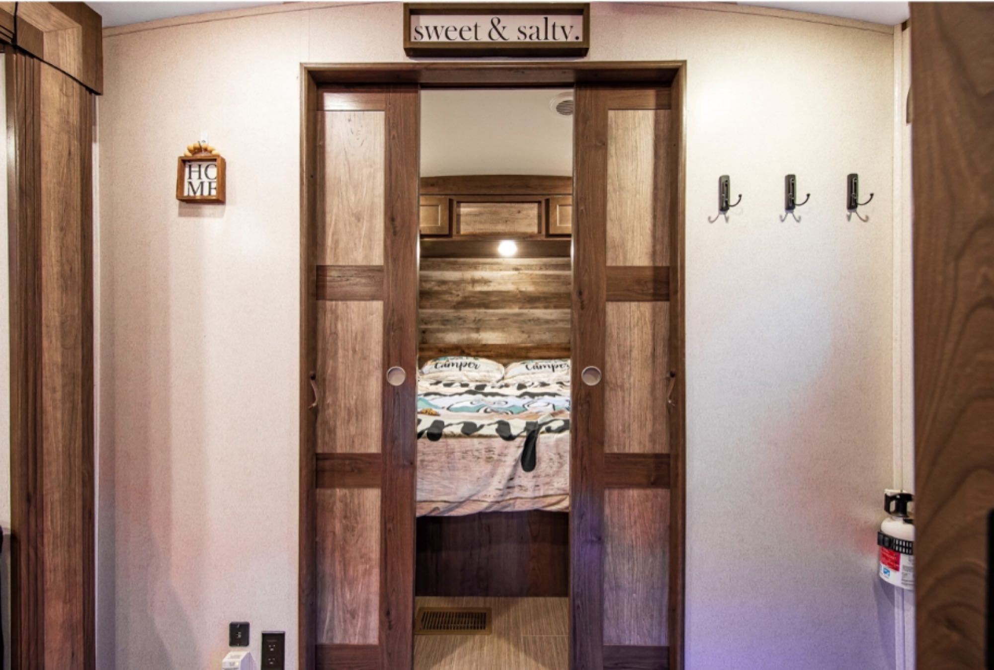 RV rental interior: Bedroom with wood sliding doors, a comfy bed, "sweet & salty" sign, and practical hooks.. Keystone RV Passport GT 2021