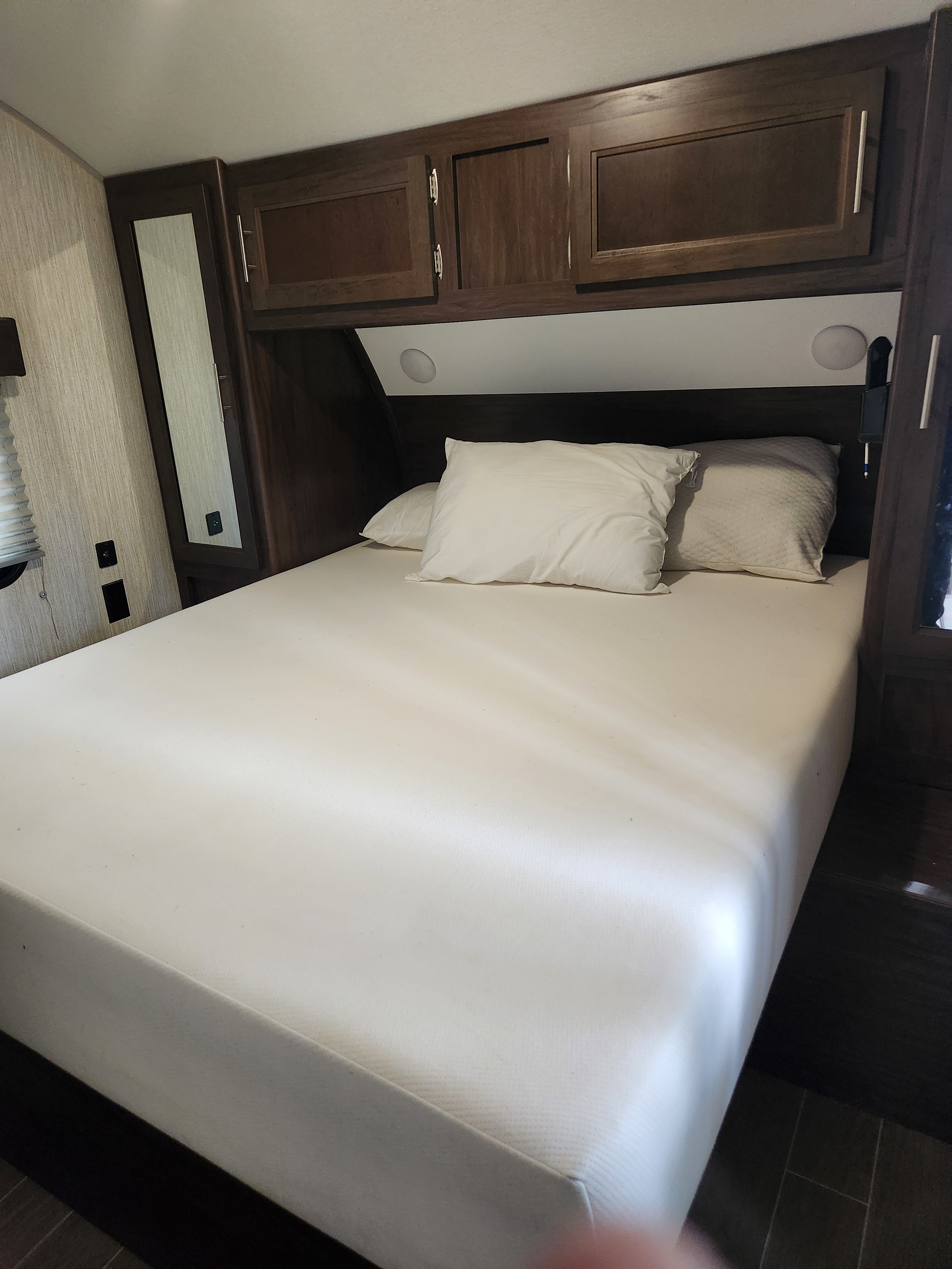 Inside an RV rental: a compact bedroom featuring a white mattress, pillows, and dark wood built-in storage.. Forest River Cherokee 2020