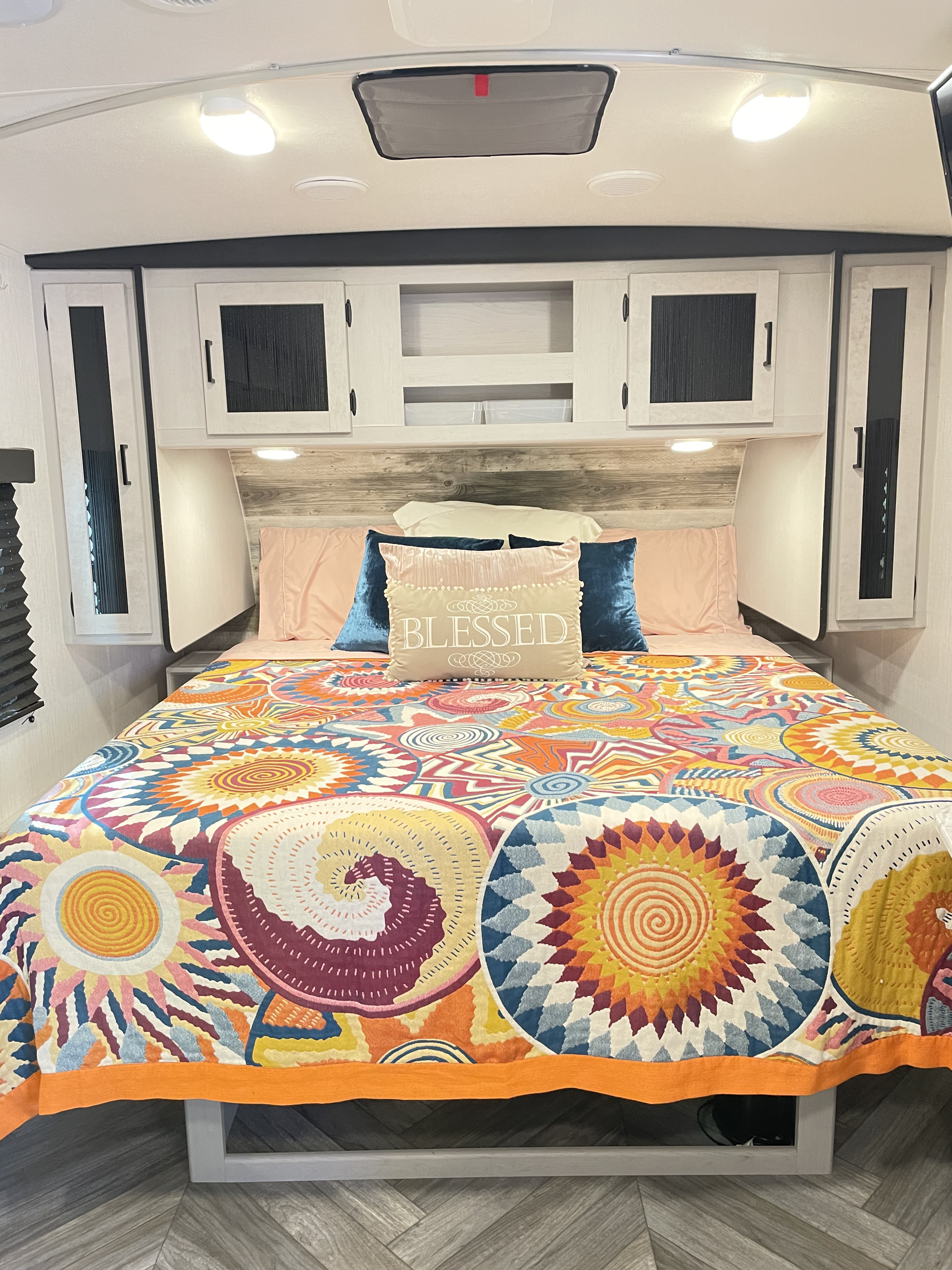 Colorful and cozy RV bedroom with a vibrant patterned quilt, "Blessed" pillow, and overhead storage. Great for an rv rental.. Heartland RVs Mallard 2023