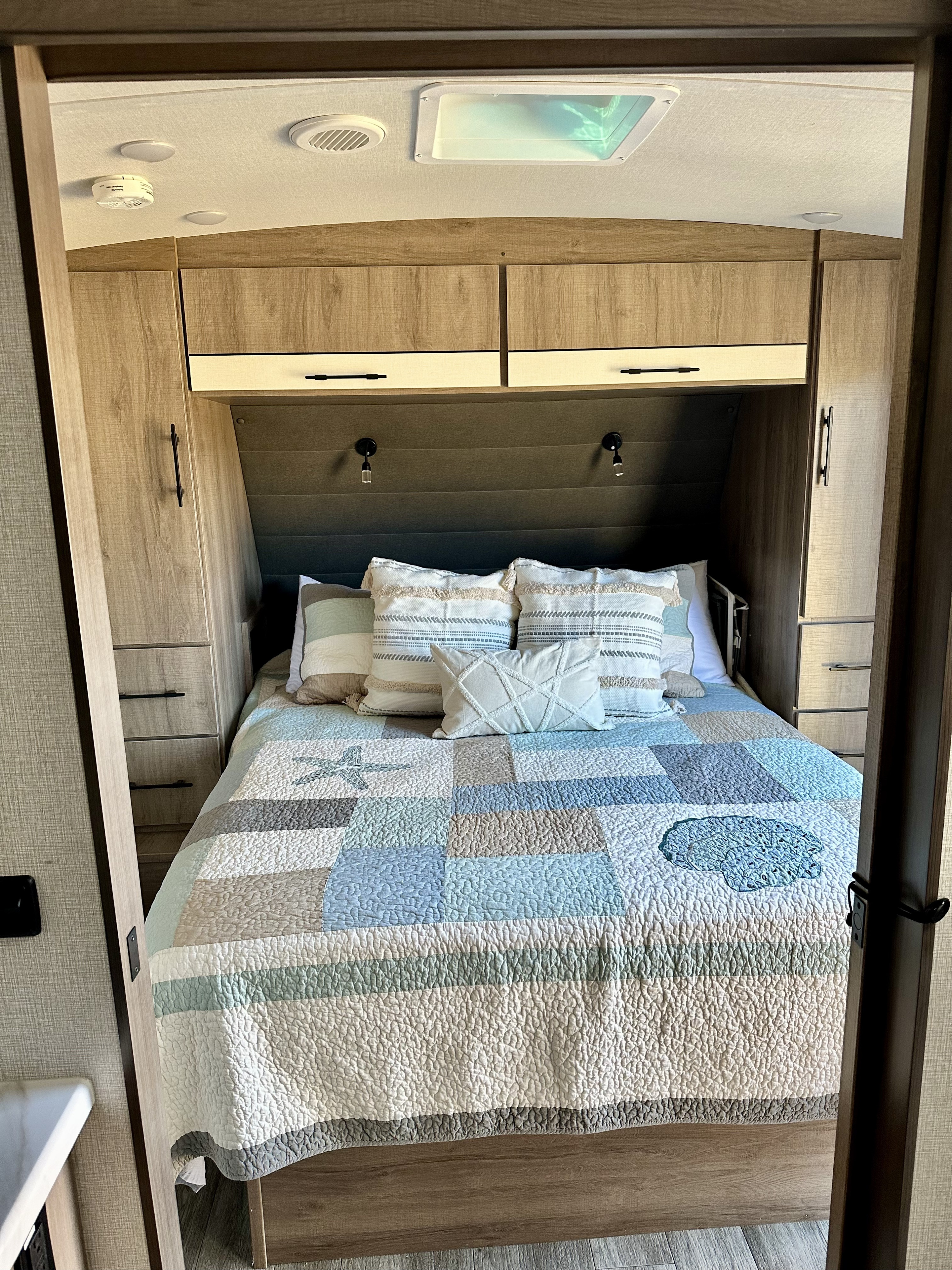Inviting RV rental bedroom with patchwork quilt, built-in storage, reading lights, and ceiling skylight. Ready for travel.. Grand Design Imagine 2023
