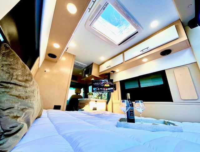 Step inside this luxurious RV rental: a plush bed with wine, TV, skylight, and overhead lighting for comfort and style.. Regency Xalta 2022