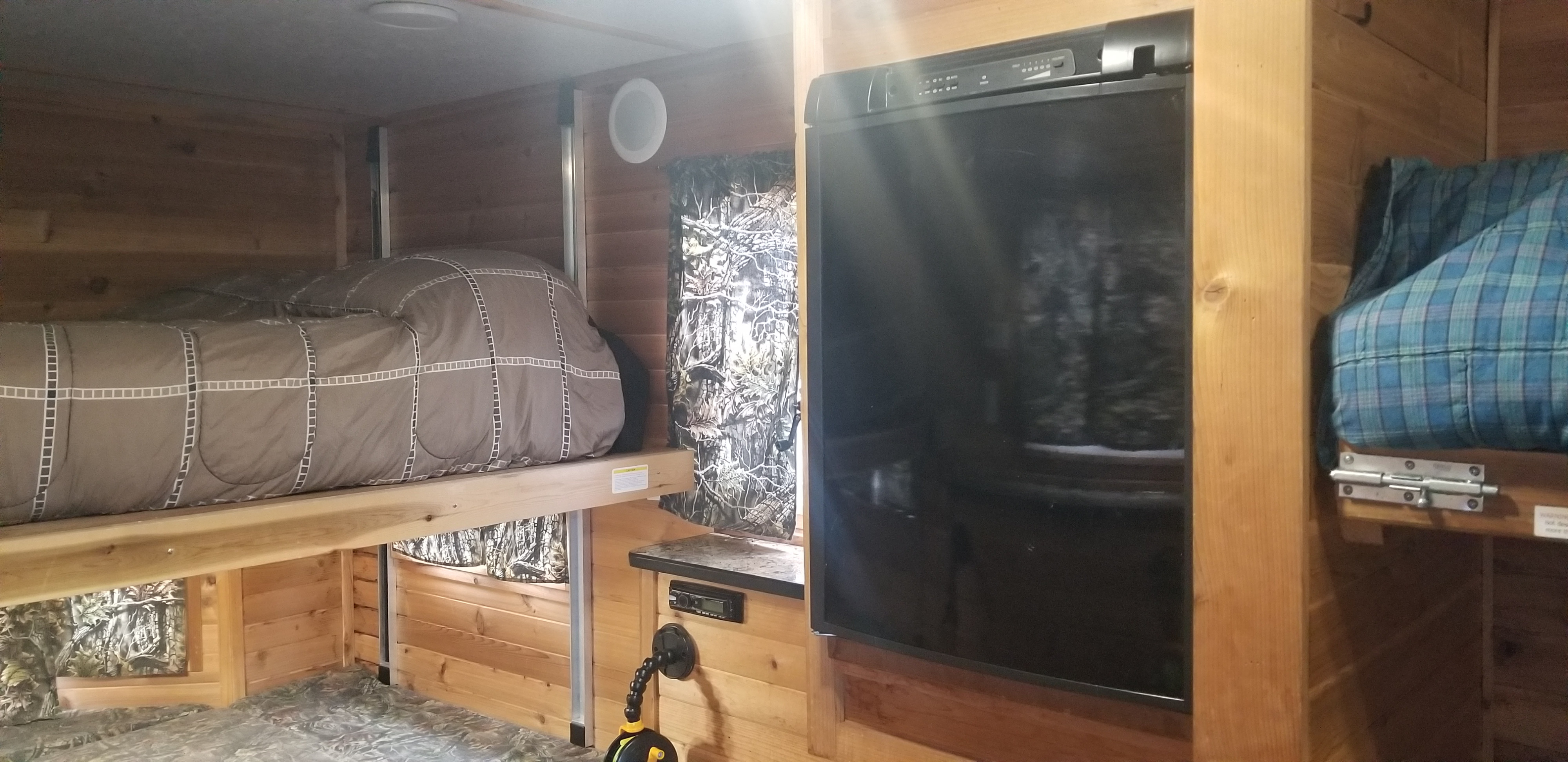 Inside an RV rental: a compact, wood-paneled interior with comfortable bunk beds, a refrigerator, and an entertainment system.. Ice Castle Fish Houses Ice Castle Fish Houses Trailer 2016