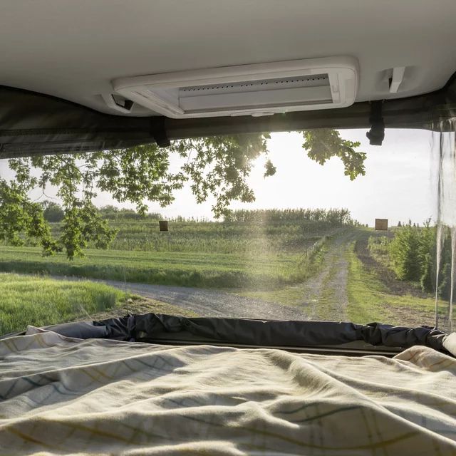 Cozy RV rental bed overlooks winding rural road and sunlit fields. Perfect nature view.. Hymer Grand Canyon 2024