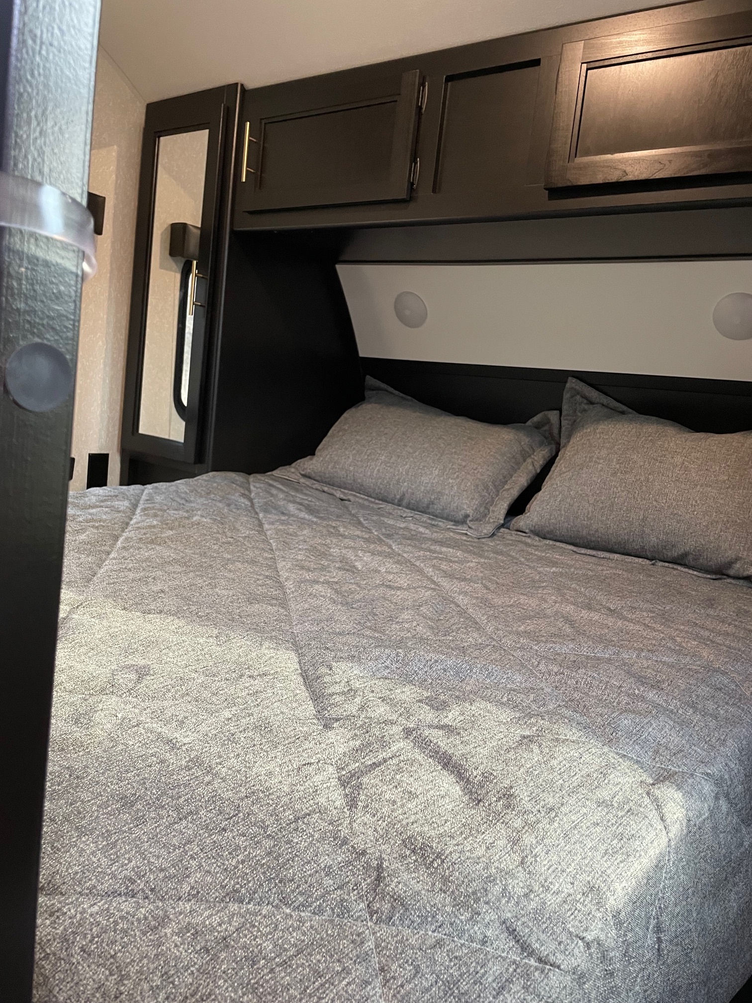 Cozy RV rental bedroom featuring gray bedding, dark overhead cabinets, and a built-in mirror for a comfortable sleeping area.. Forest River Cherokee 2022