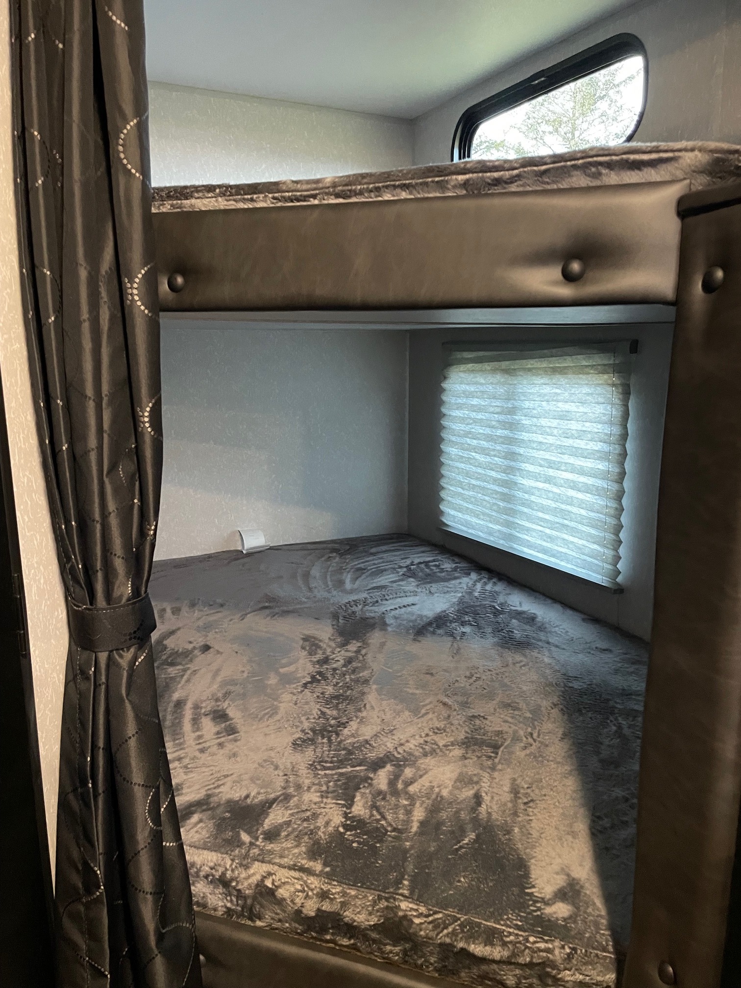 An RV rental's bunkhouse with dark curtains, a top bunk window, and a lower bunk with window blinds.. Forest River Cherokee 2022