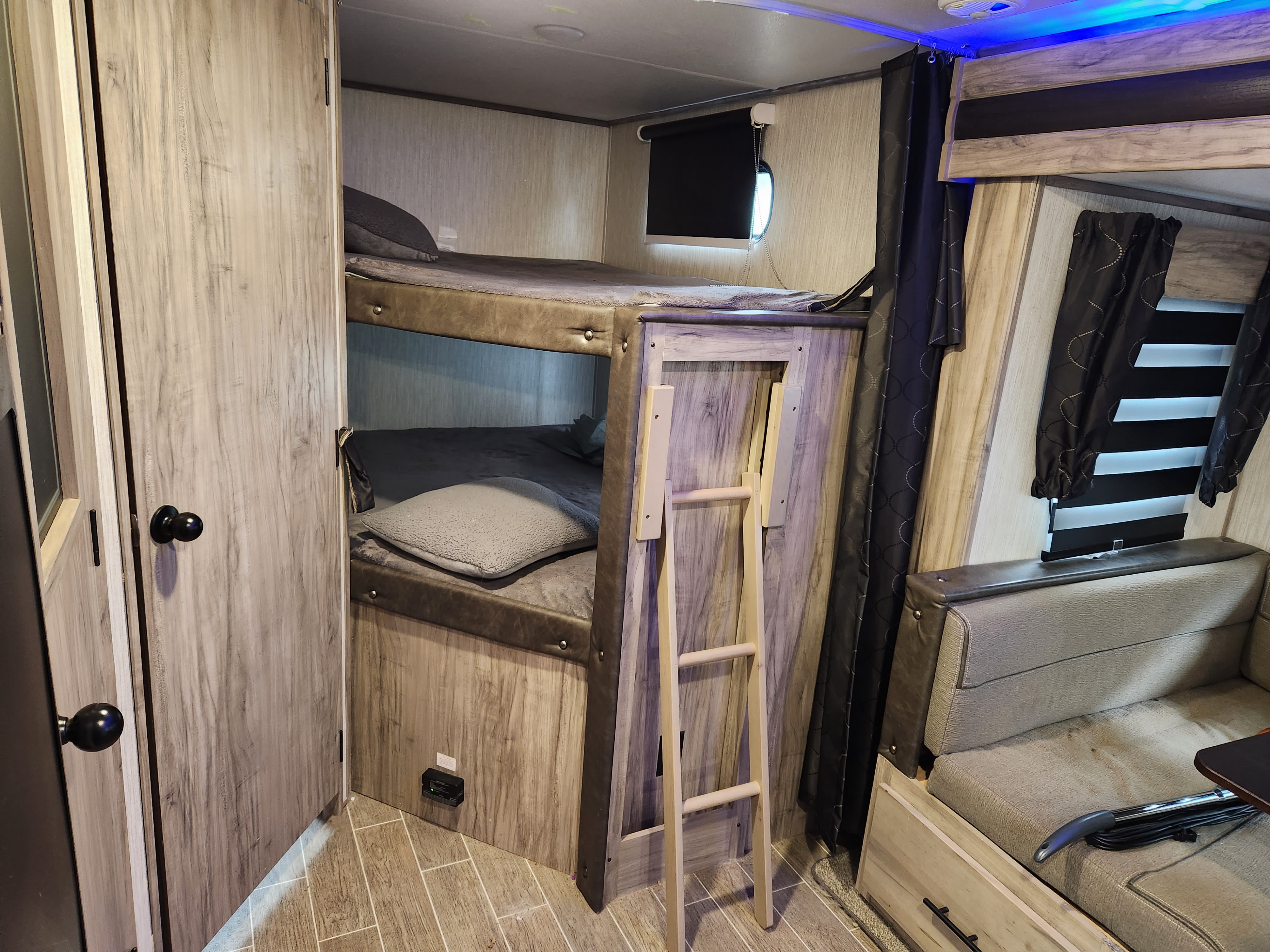 RV rental interior: bunk beds with ladder, compact sleeping/living space, modern wood-grain finishes and blue LED accents.. Forest River Cherokee Alpha Wolf 2020