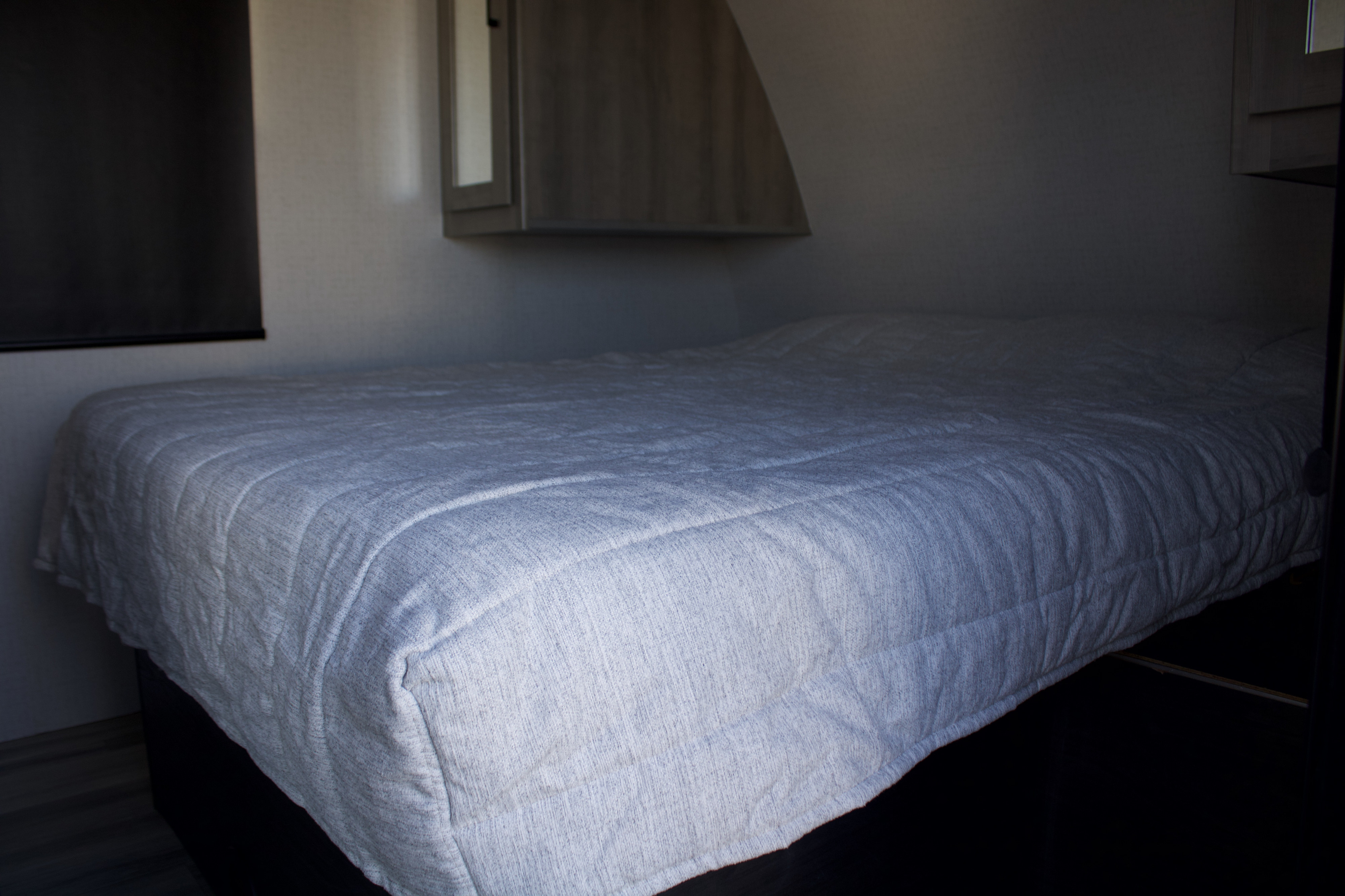 Cozy RV rental bedroom featuring a comfortable bed with a quilted spread, compact overhead storage, and a blackout blind.. Winnebago Voyage 2022