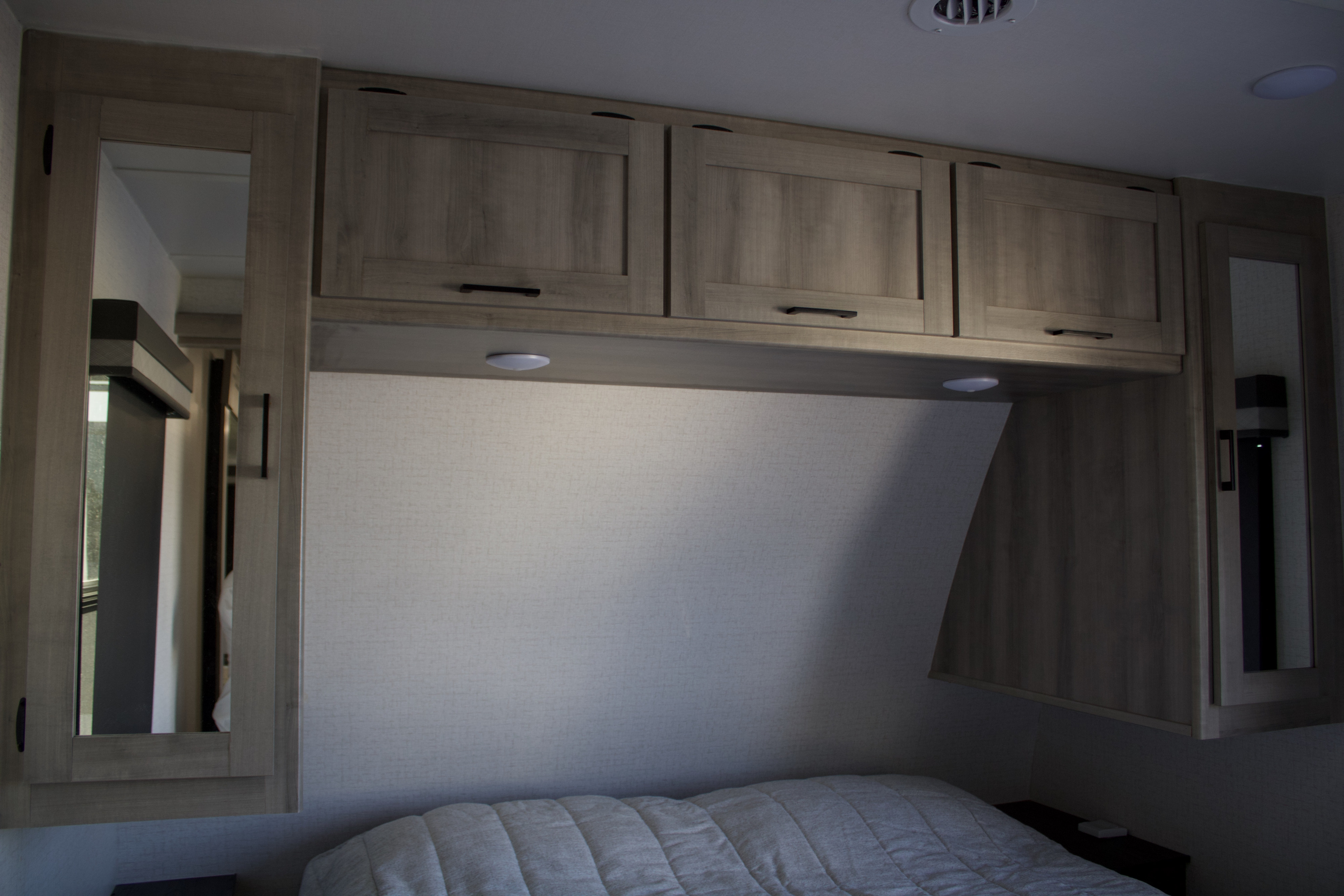 Built-in wooden cabinets & mirrored storage in a functional rv rental bedroom. Features under-cabinet lights over a cozy bed.. Winnebago Voyage 2022