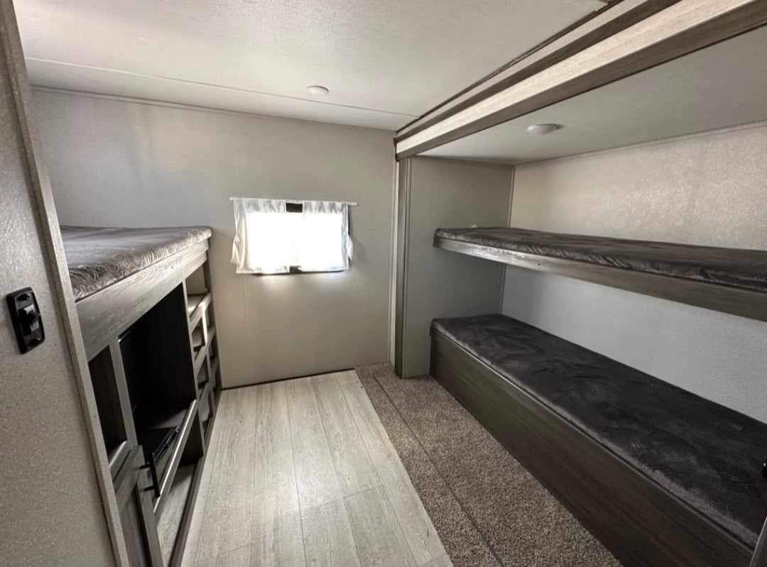 This RV rental bunkhouse features multiple bunk beds, a TV unit, and mixed flooring. Ideal for family travel accommodation.. Shasta 32DS 2021