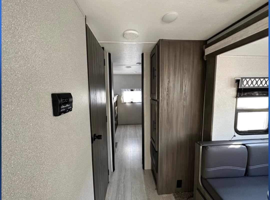 RV rental interior: A narrow hallway leads past a control panel & storage to a bunk area, with seating & windows visible.. Shasta 32DS 2021