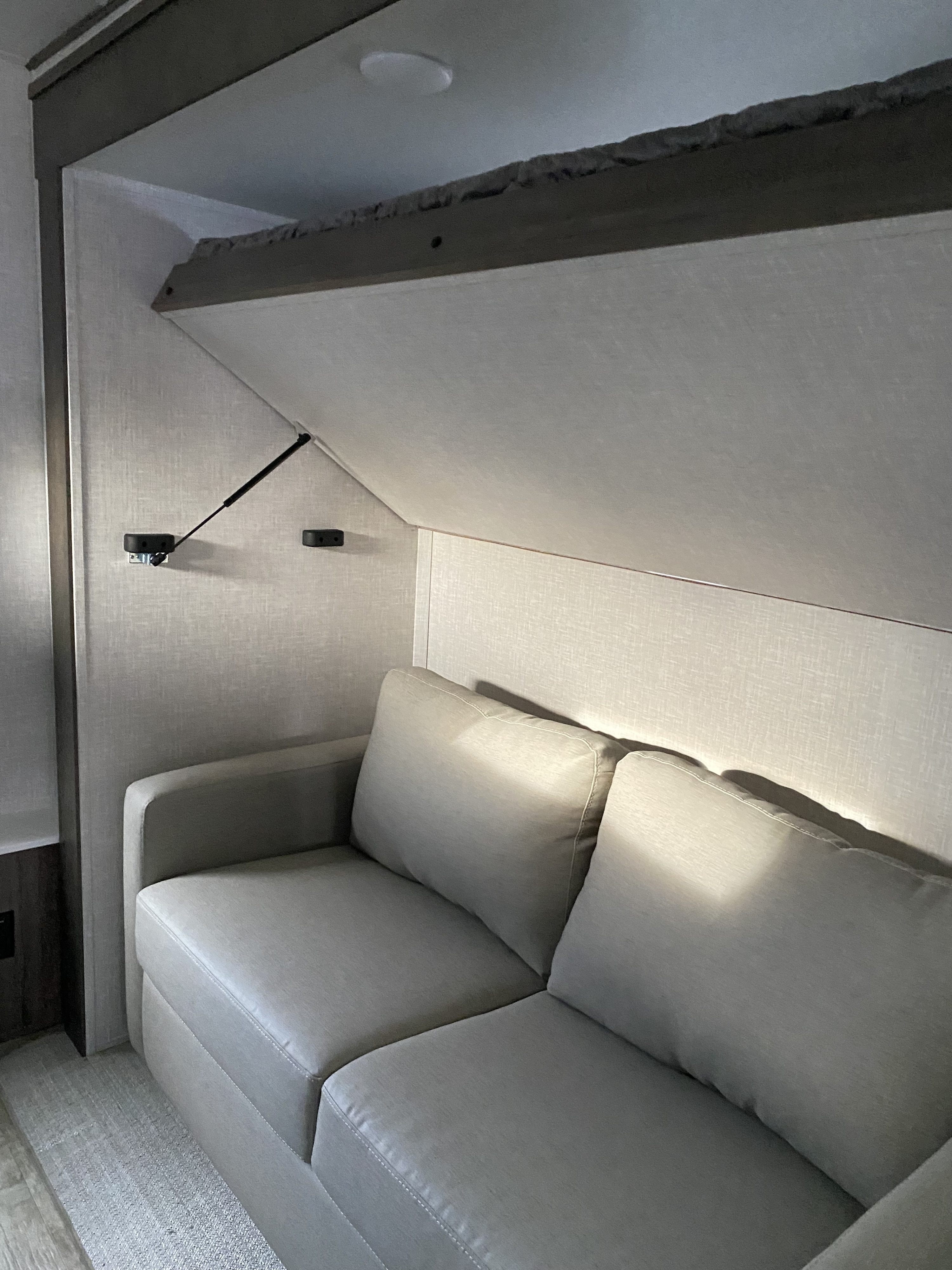 RV rental interior featuring a cozy sofa with an innovative fold-down upper bunk or storage area, designed for compact living.. Forest River Flagstaff Classic 2023