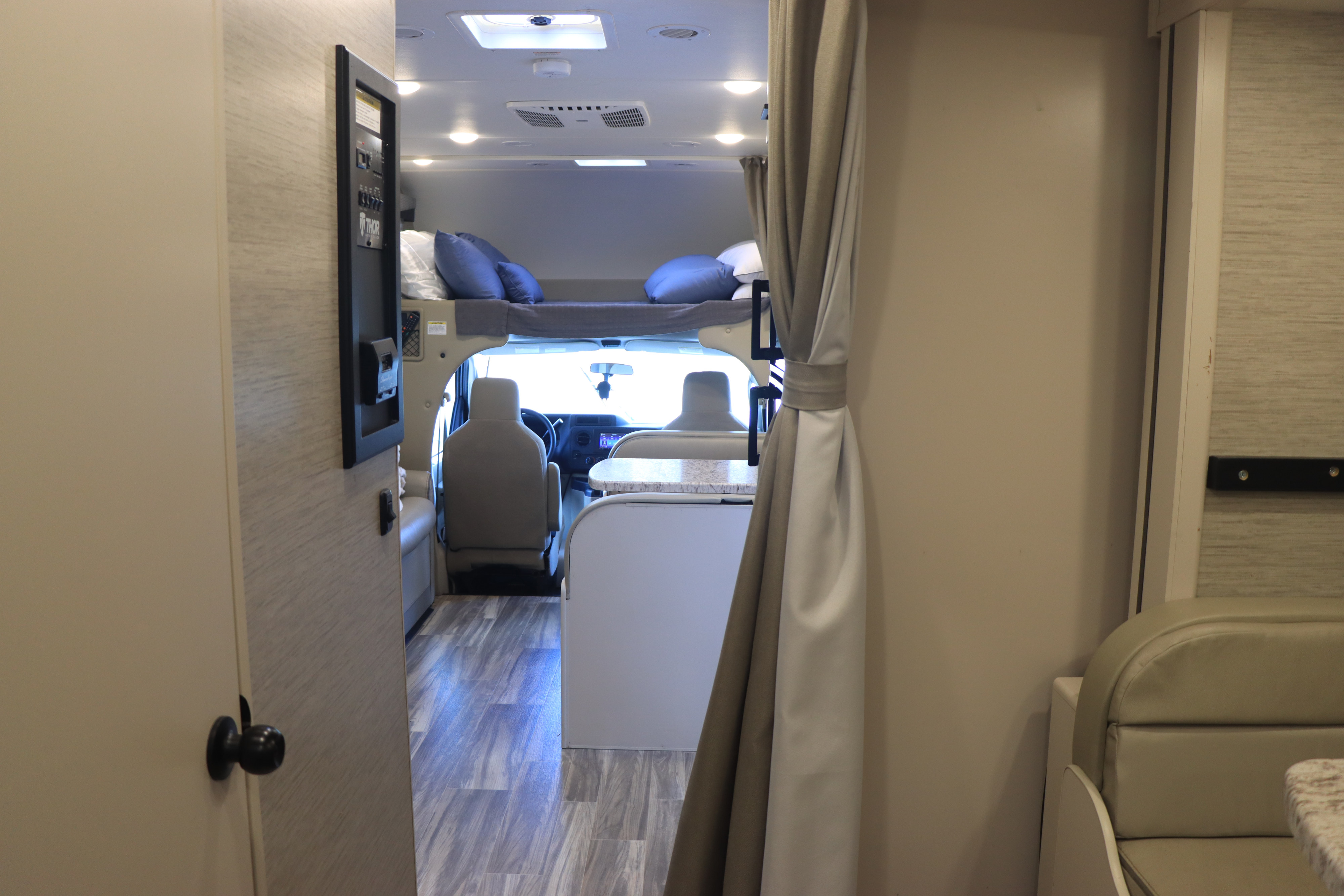 Interior of an RV rental showing the cab, overhead bunk with blue pillows, and dinette area.. Thor Freedom Elite 2023