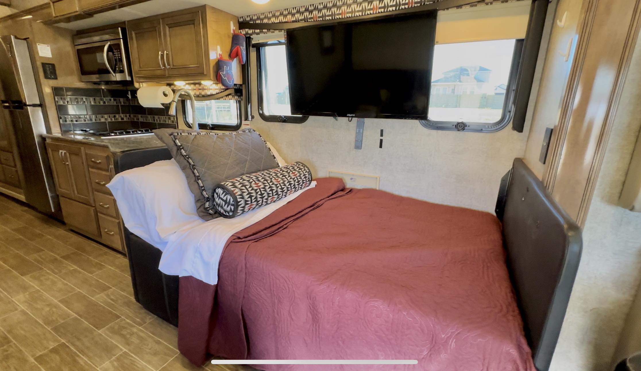 Inside an RV rental: a compact living space featuring a bed with red quilt, wall-mounted TV, and kitchen area.. Thor Outlaw 2020