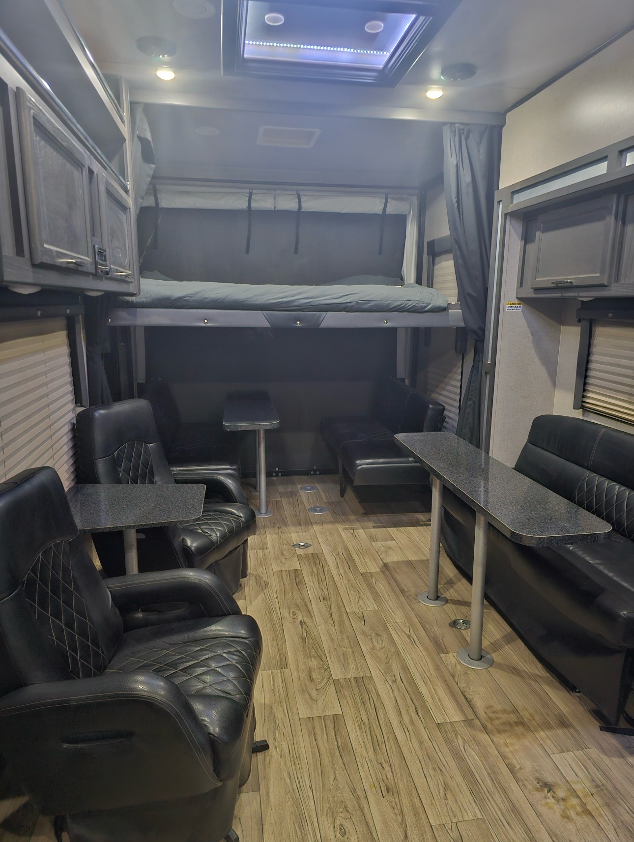 Spacious RV rental interior featuring flexible seating, tables, wood-look flooring, and an elevated bunk bed system.. Genesis Supreme Rv Genesis Supreme 2019