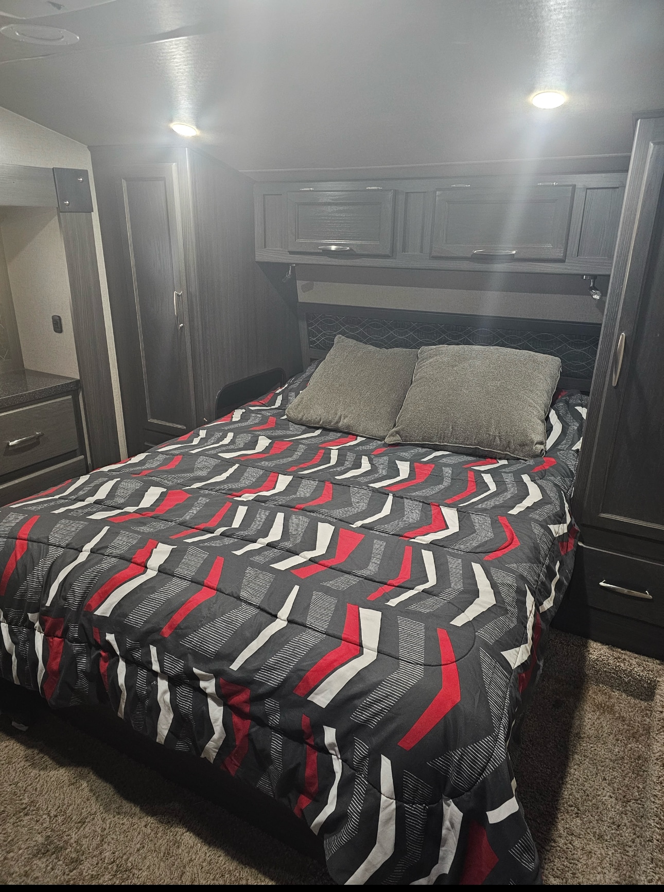 Cozy RV rental bedroom with patterned comforter, grey pillows, and built-in storage. Ideal for travel comfort.. Genesis Supreme Rv Genesis Supreme 2019