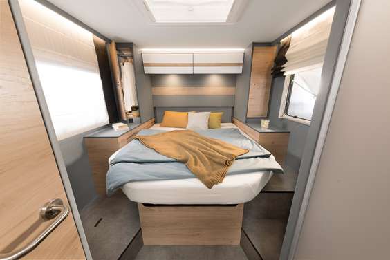 Modern RV rental bedroom with compact bed, wood accents, and integrated storage units.. Dethleffs Just T7052 DBM 2024