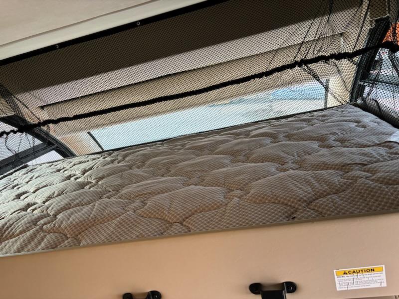 Inside an RV rental, an overhead bunk bed features a quilted mattress and safety net. Ideal for comfortable travel sleeping.. Thor Vegas 2018