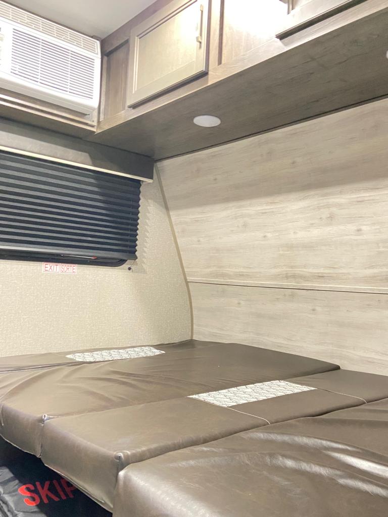RV rental interior: A sleeping area with brown cushions, AC, window with blinds, and wooden cabinets.. Jayco Jay Flight SLX 2021