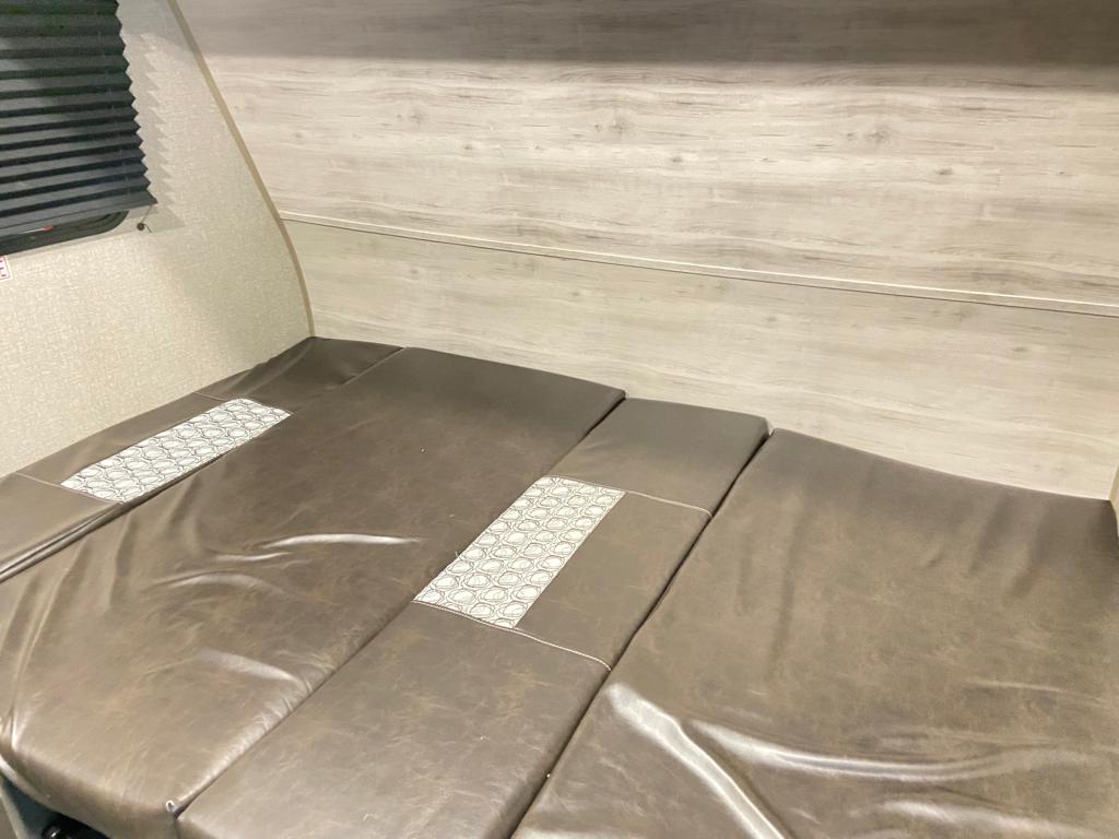 Cozy RV rental interior with a brown cushioned convertible bed/dinette. Wood-grain walls and window blinds add comfort.. Jayco Jay Flight SLX 2021