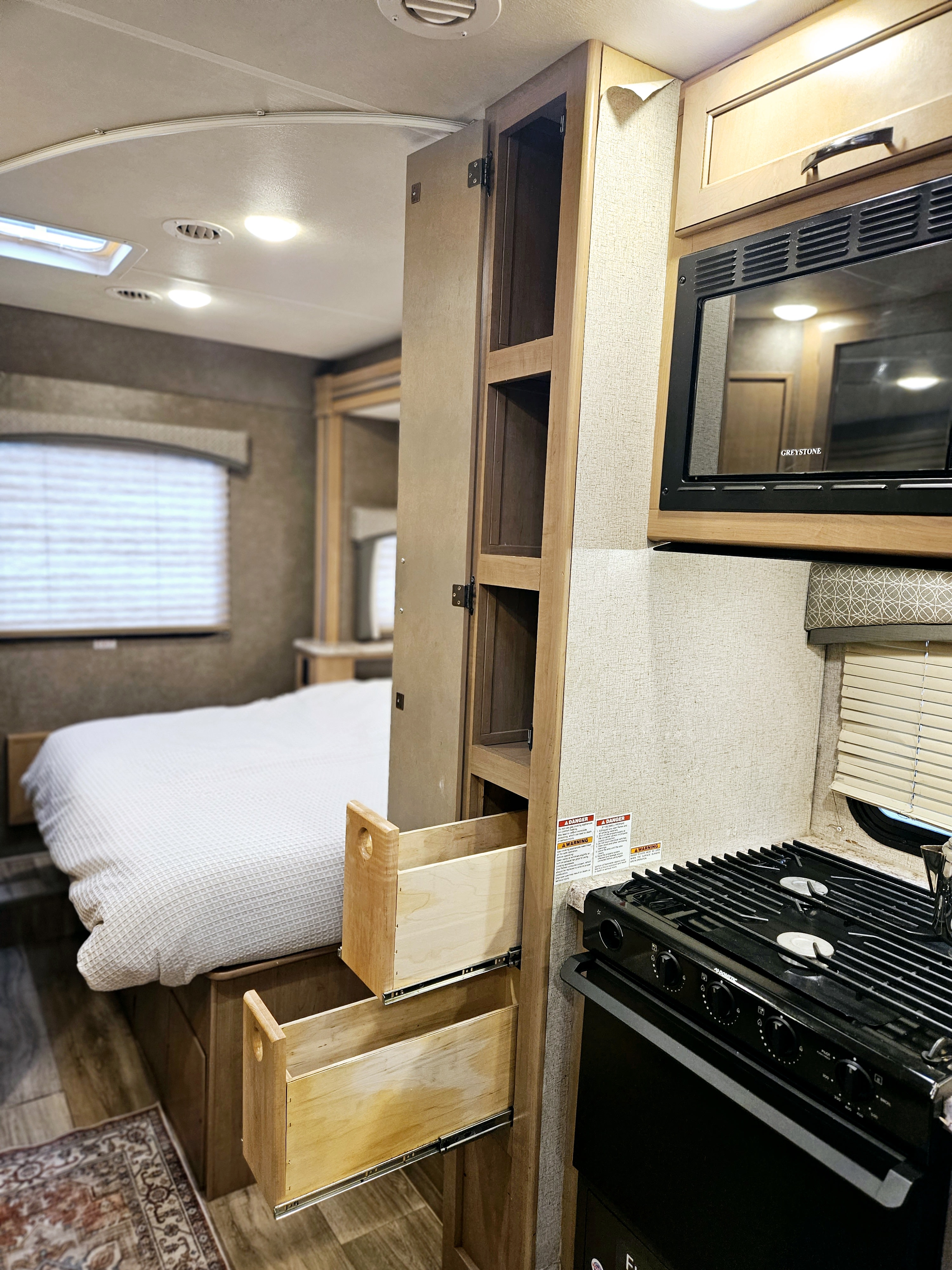 Inside a comfortable RV rental: kitchen with stove & microwave, plus bedroom area with open storage drawers.. Thor Motor Coach Four Winds 2021