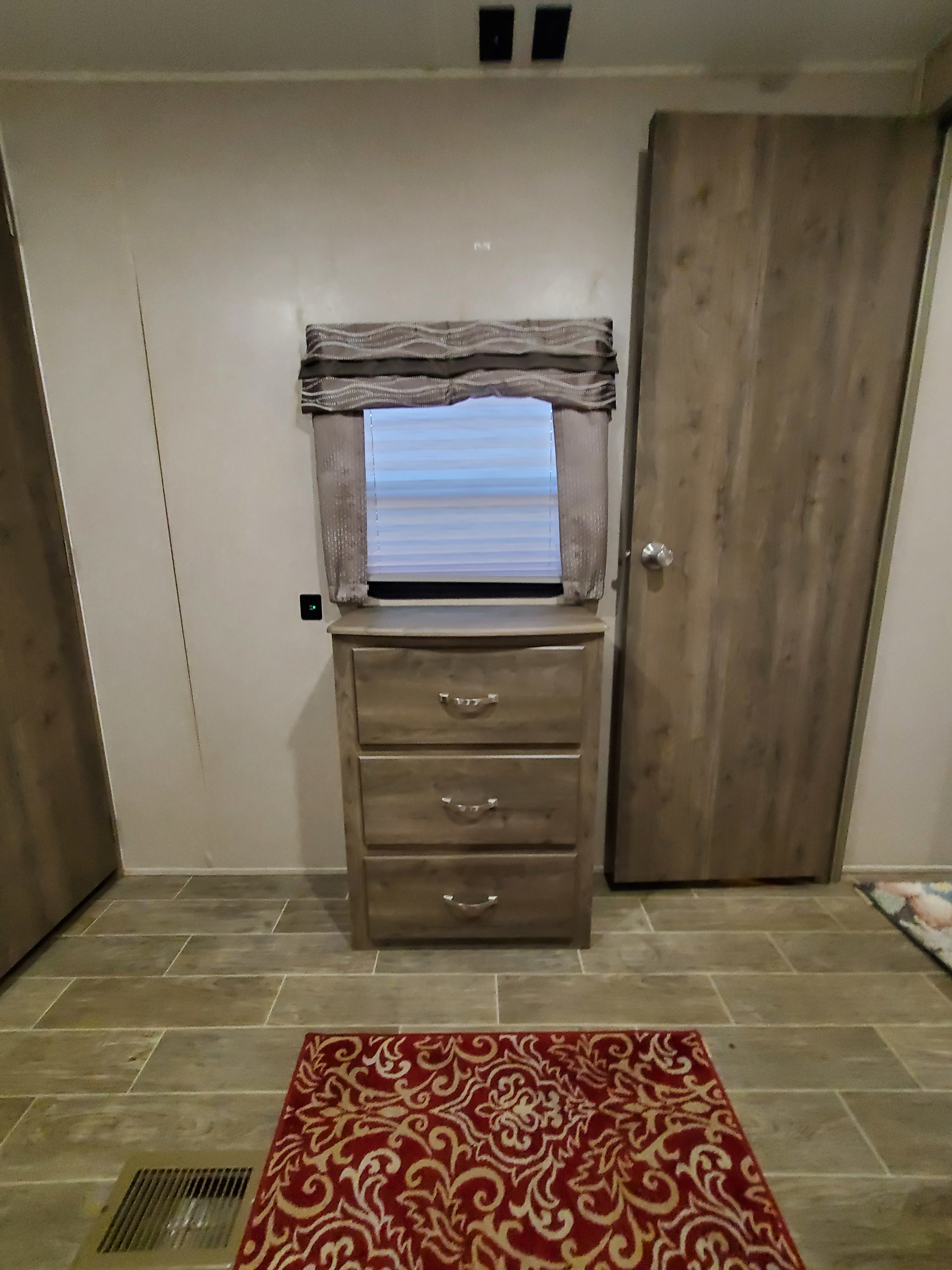 RV rental interior view: compact bedroom area with a dresser, window with blinds, wood-look doors, and a decorative rug on tiled floor.. Palomino Puma 2019