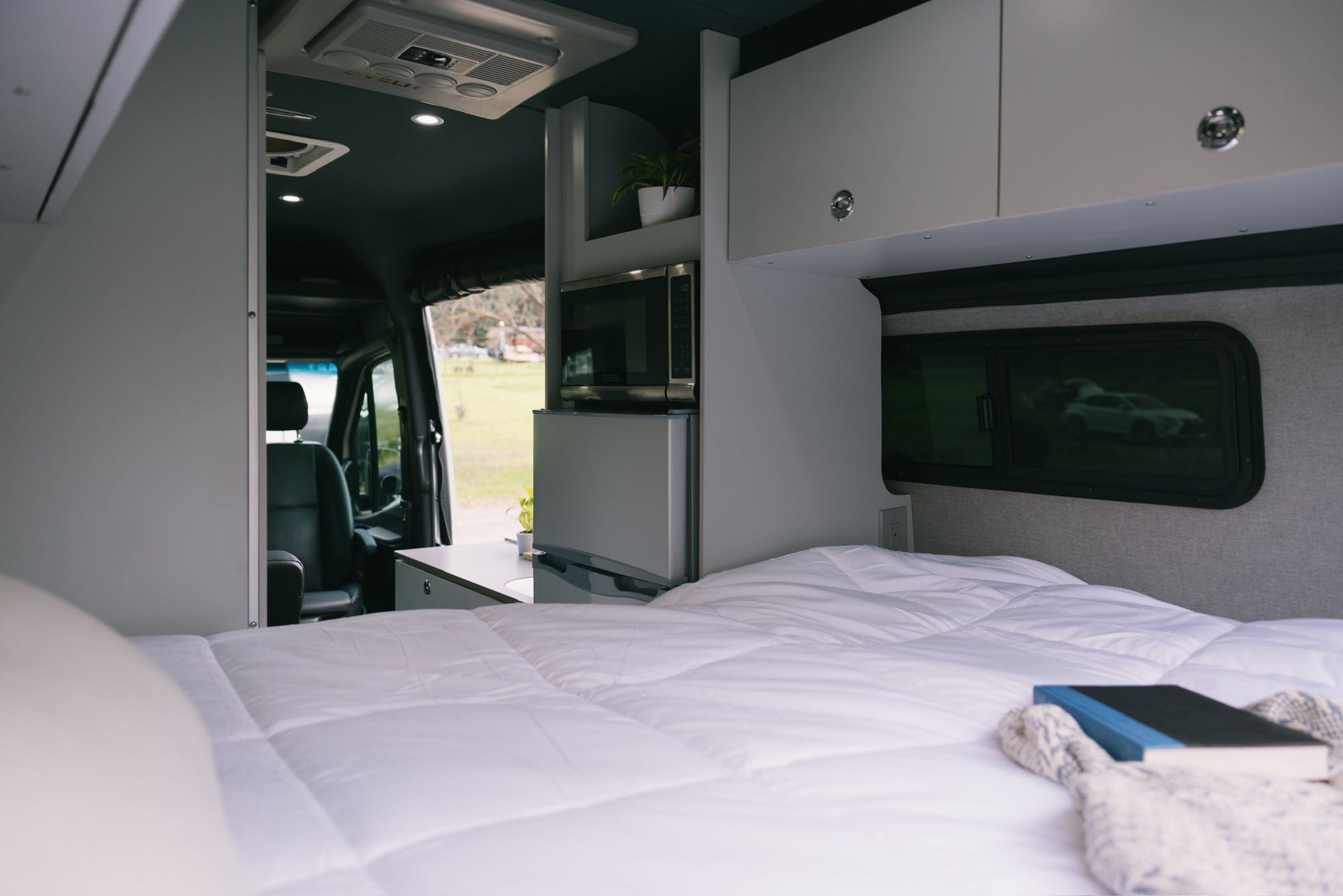 Experience an RV rental: interior with a cozy bed, compact kitchen (microwave, fridge), and driver's cab.. Mercedes-Benz Sprinter 2021