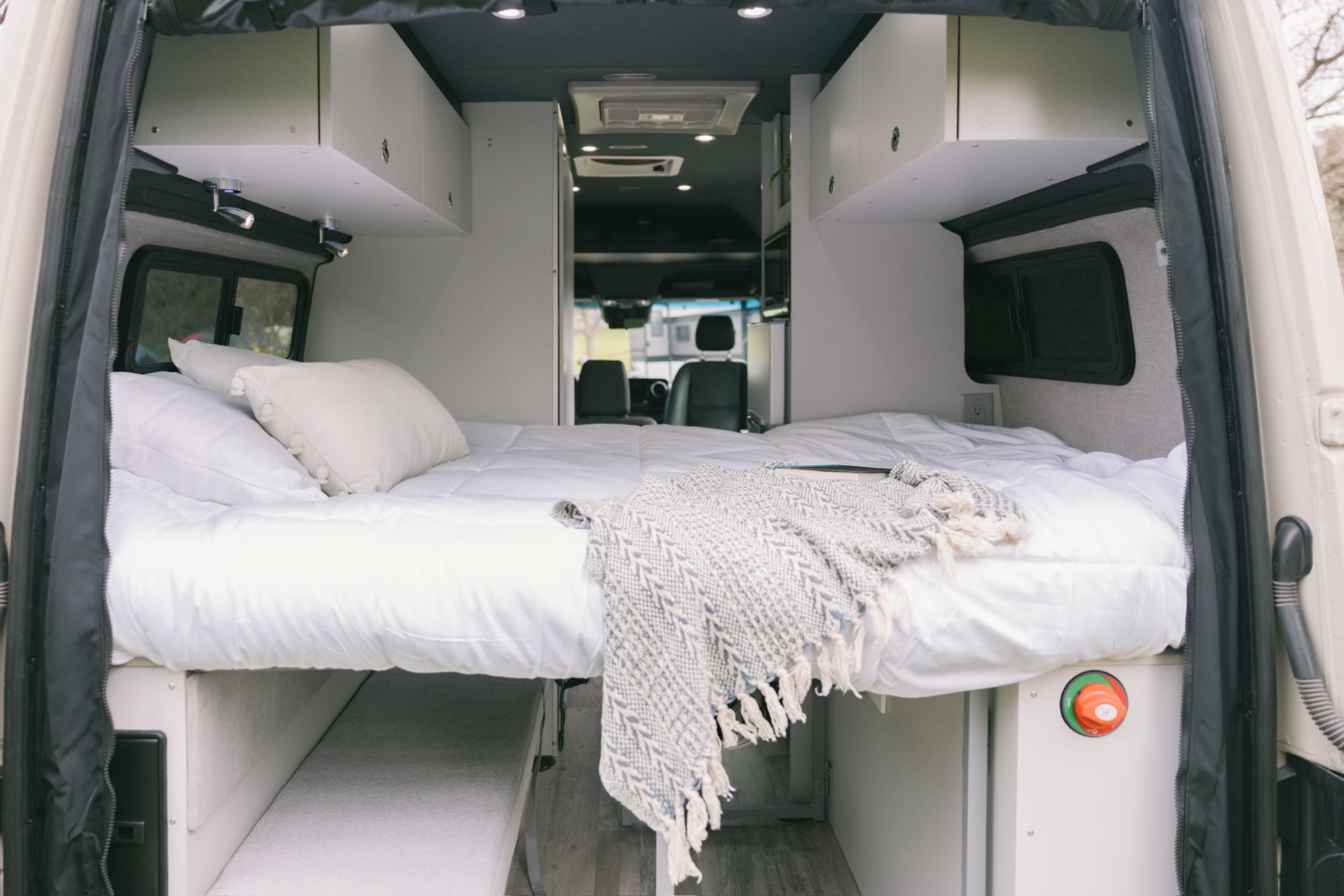 Comfortable RV rental camper van interior. Features a cozy bed, overhead storage, and windows for your road trip.. Mercedes-Benz Sprinter 2021