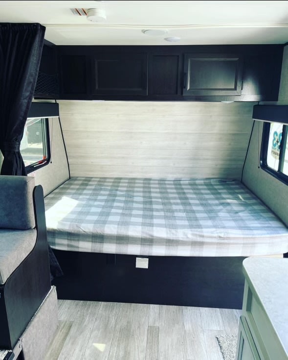 RV rental interior shows a cozy, compact space with a plaid-covered bed, dark cabinets, and windows. Light wood-look walls complete the scene.. Jayco Jay Flight SLX Baja Edition 2023
