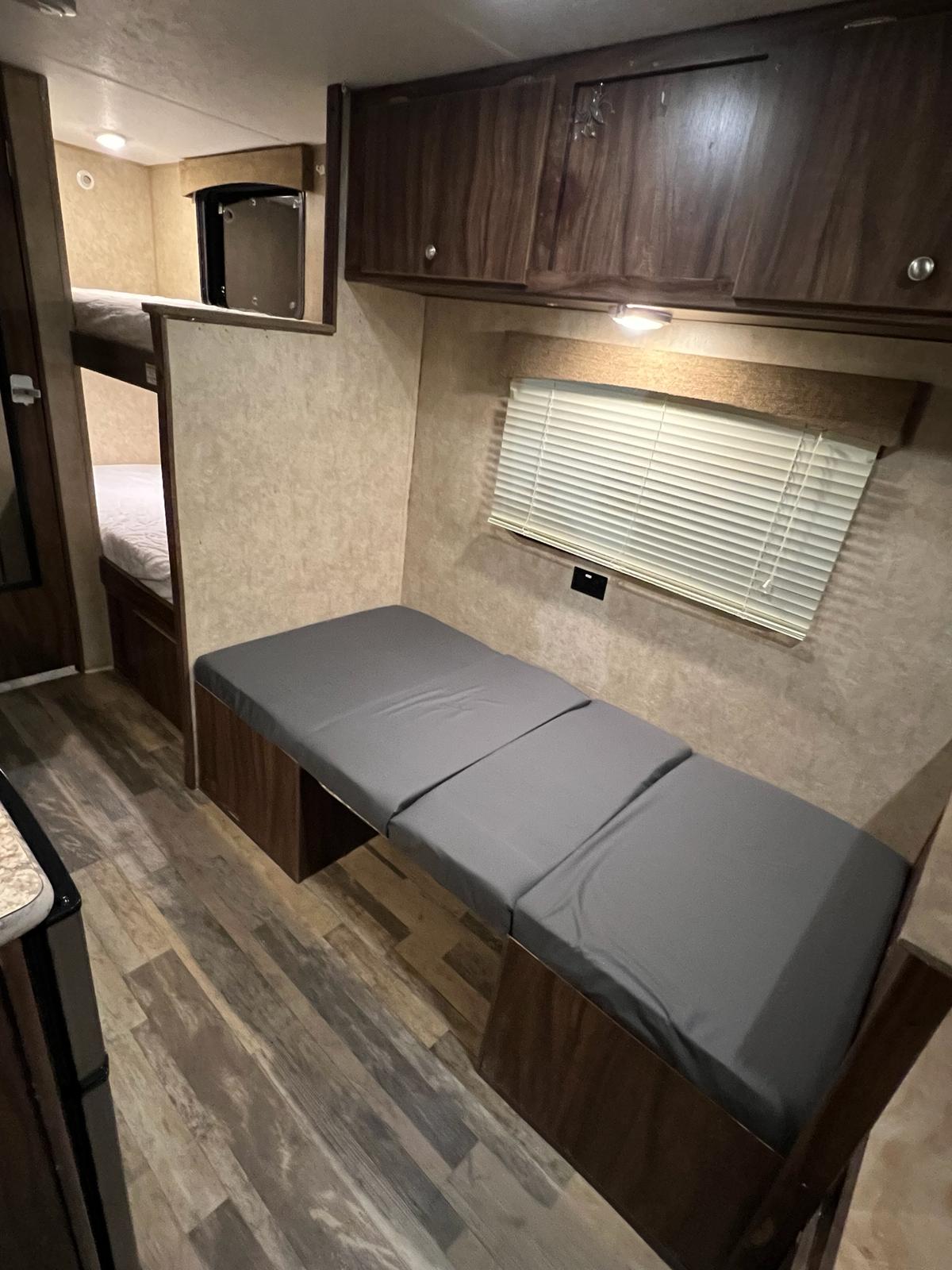 RV rental interior featuring bunk beds, a convertible bench, overhead cabinets, and a window.. Coachmen Viking 2018