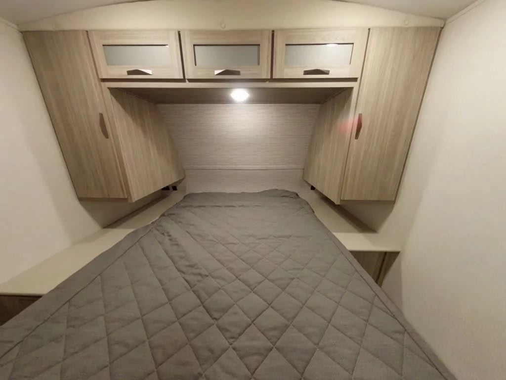 Cozy RV rental bedroom featuring a comfortable bed, frosted overhead cabinets, and angled side wardrobes for storage.. Keystone Passport 2024