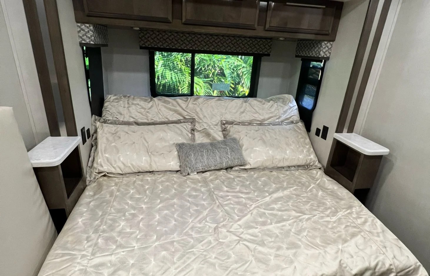 Cozy RV rental bedroom with light bedding, pillows, nightstands, and a window view of lush greenery.. Forest River Georgetown 7 Series 36D7 2021
