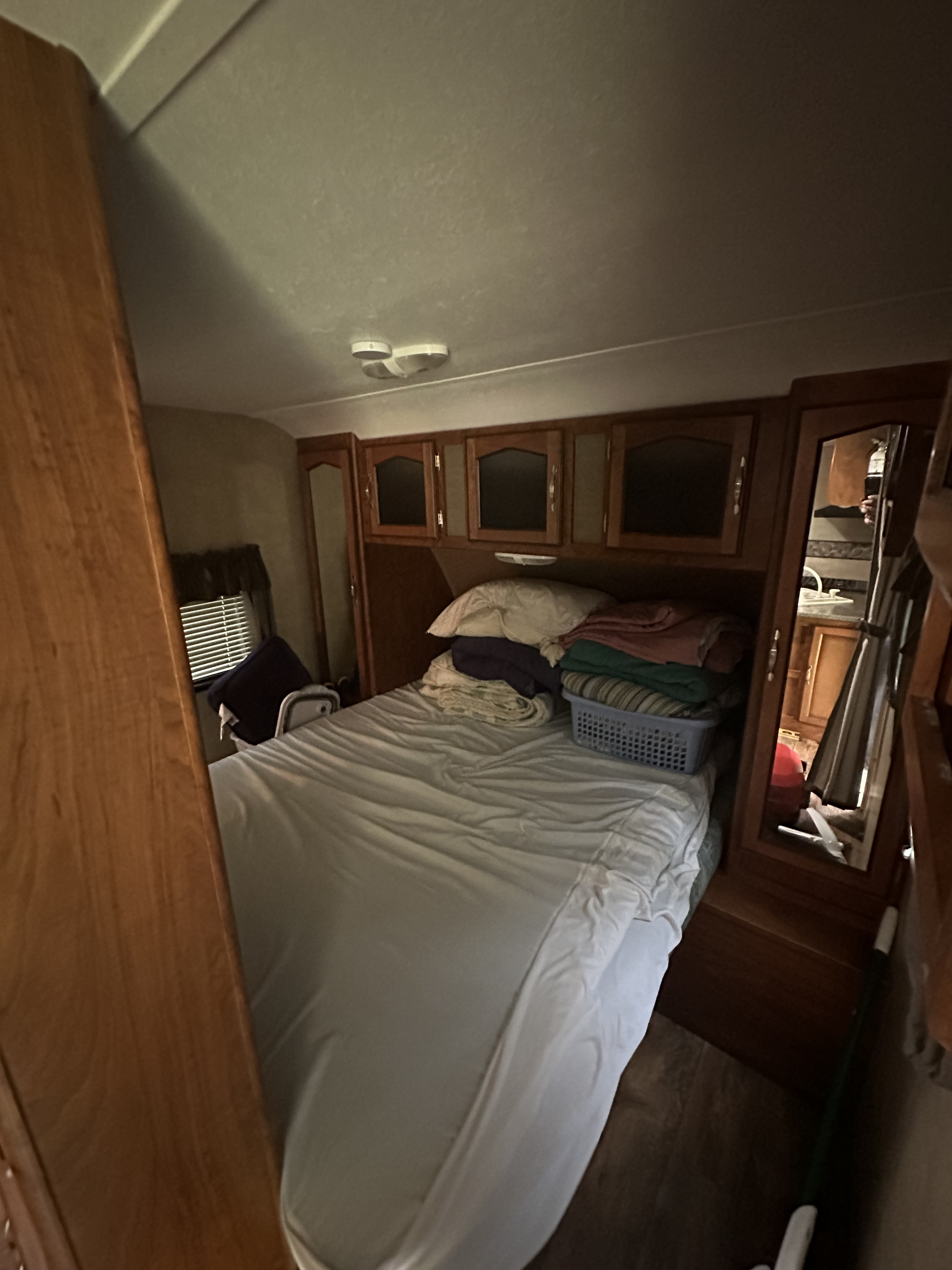 Compact RV rental bedroom showing a bed, wooden cabinets, window with blinds, and mirrored wardrobe. Ideal for travel.. Keystone RV Passport Grand Touring 2014