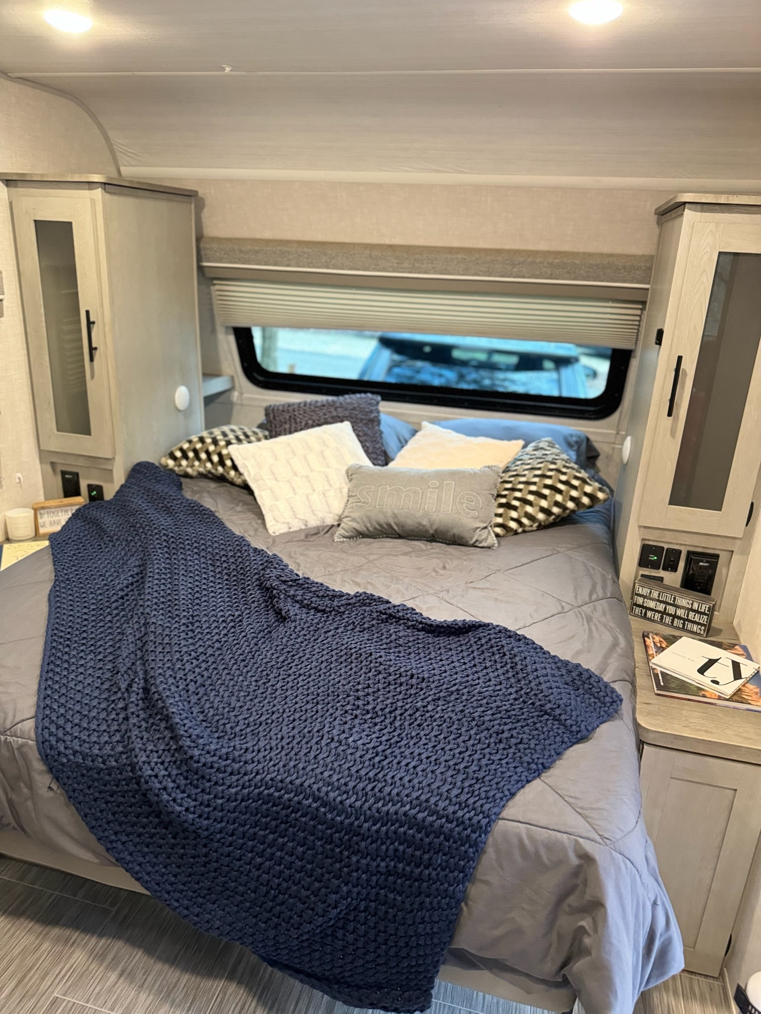 Cozy RV rental bedroom featuring a bed with gray bedding, a textured blue blanket, and integrated storage solutions.. Forest River Ibex 2021
