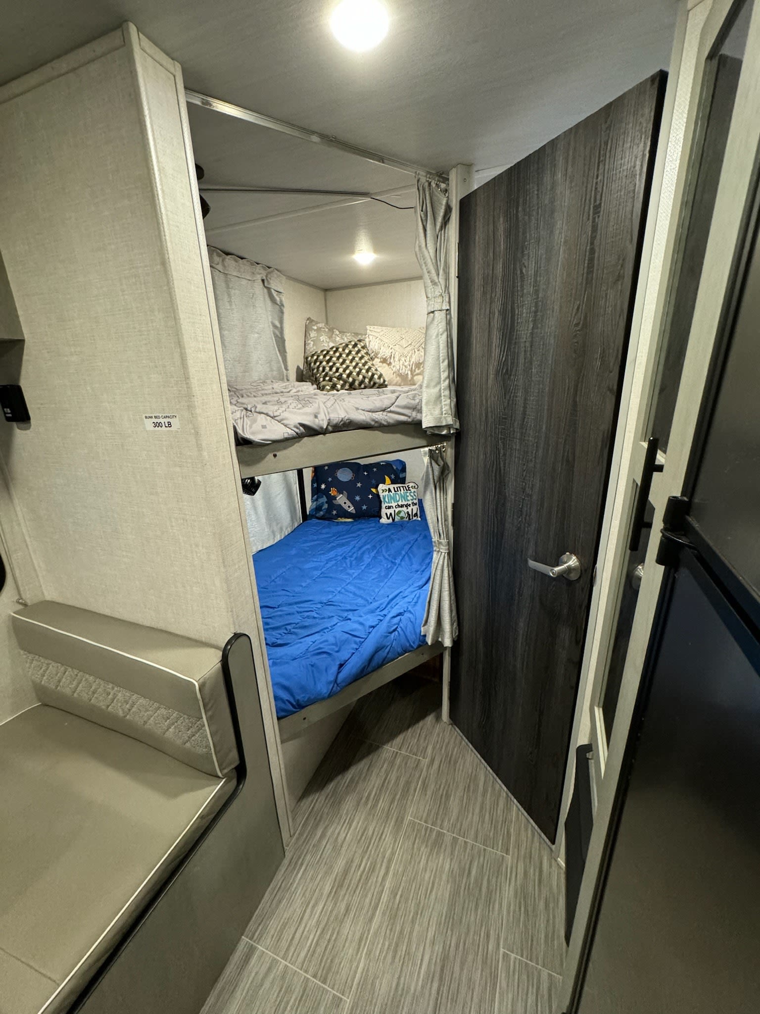 Cozy RV rental interior showcasing two-tier bunk beds with bedding, a side seating area, and private room door.. Forest River Ibex 2021