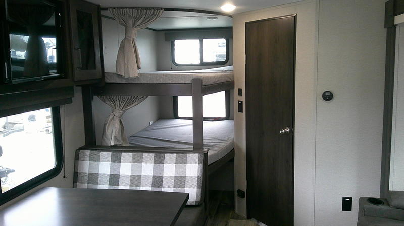 Inside an RV rental: view of bunk beds with windows and a checkered dinette, offering compact living for travel.. Grand Design Transcend 261BH 2020