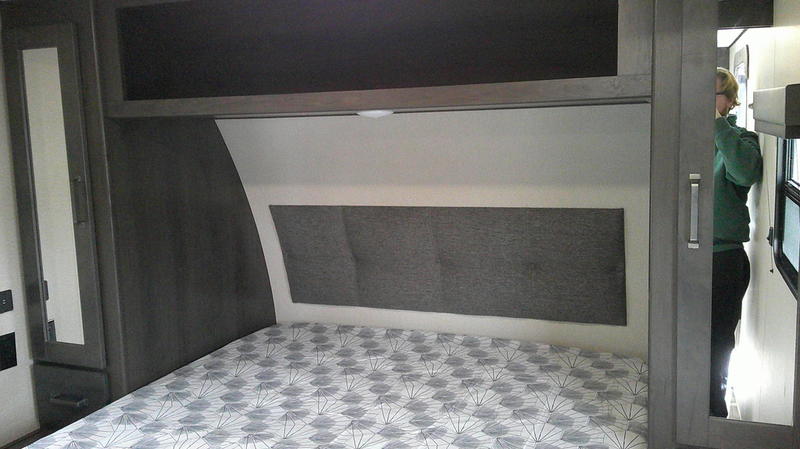 RV rental bedroom shows a bed, gray headboard, cabinets, and mirrored closet. Person visible in hallway.. Grand Design Transcend 261BH 2020