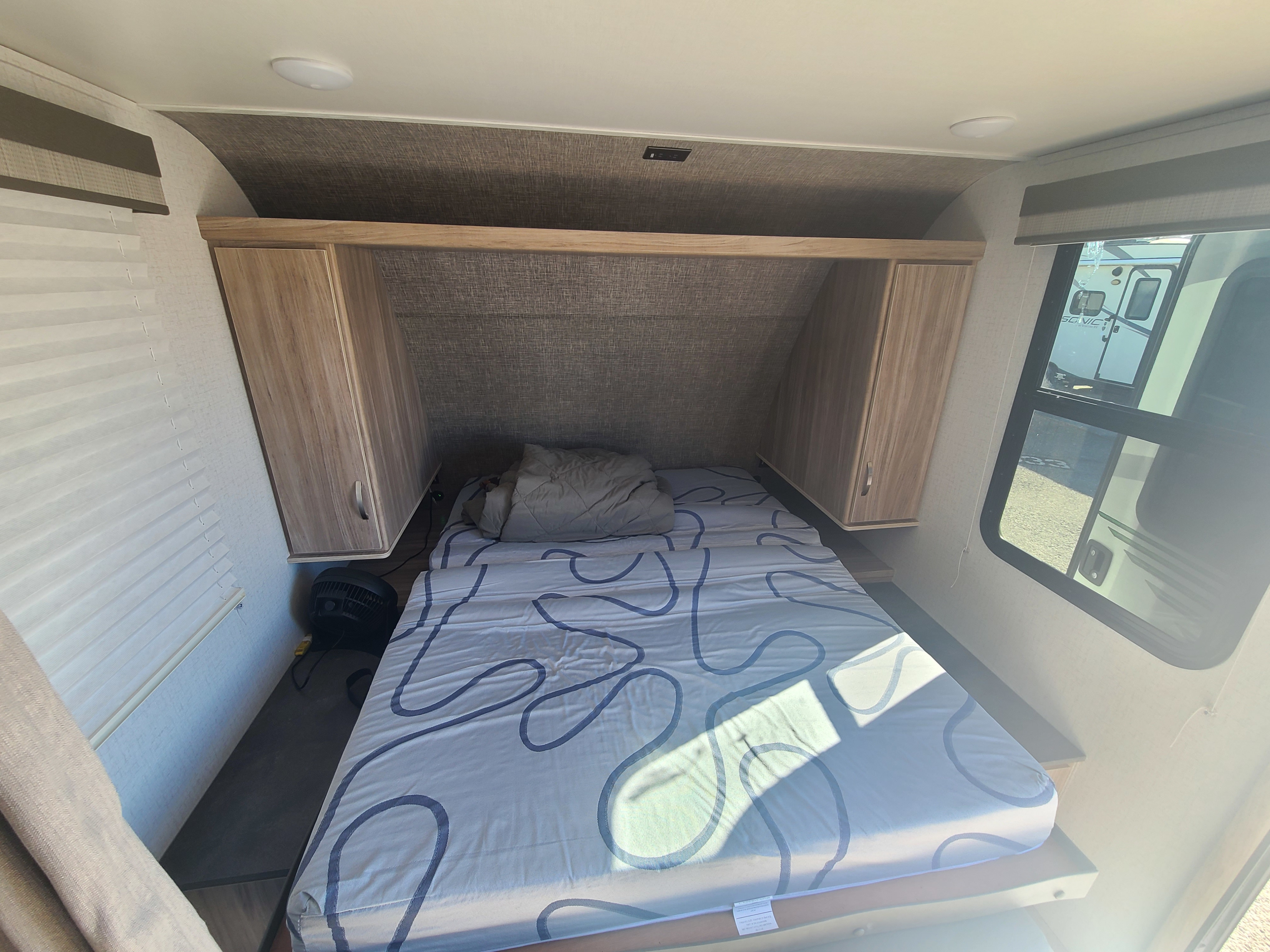 Compact RV rental bedroom with a patterned bed, overhead storage, side cabinets, and windows offering exterior views.. Winnebago Micro Minnie FLX 2022