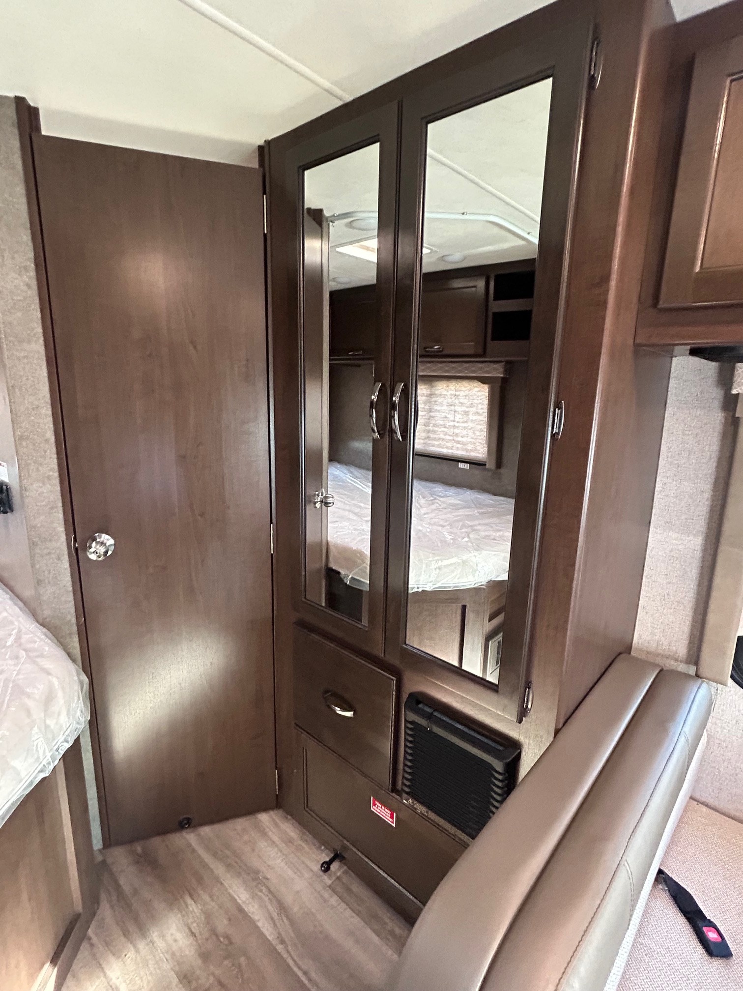Spacious RV rental interior featuring a dark wood door, mirrored wardrobe with drawers, bed, and tan seating area for travel.. Thor Freedom Elite 22HE 2020