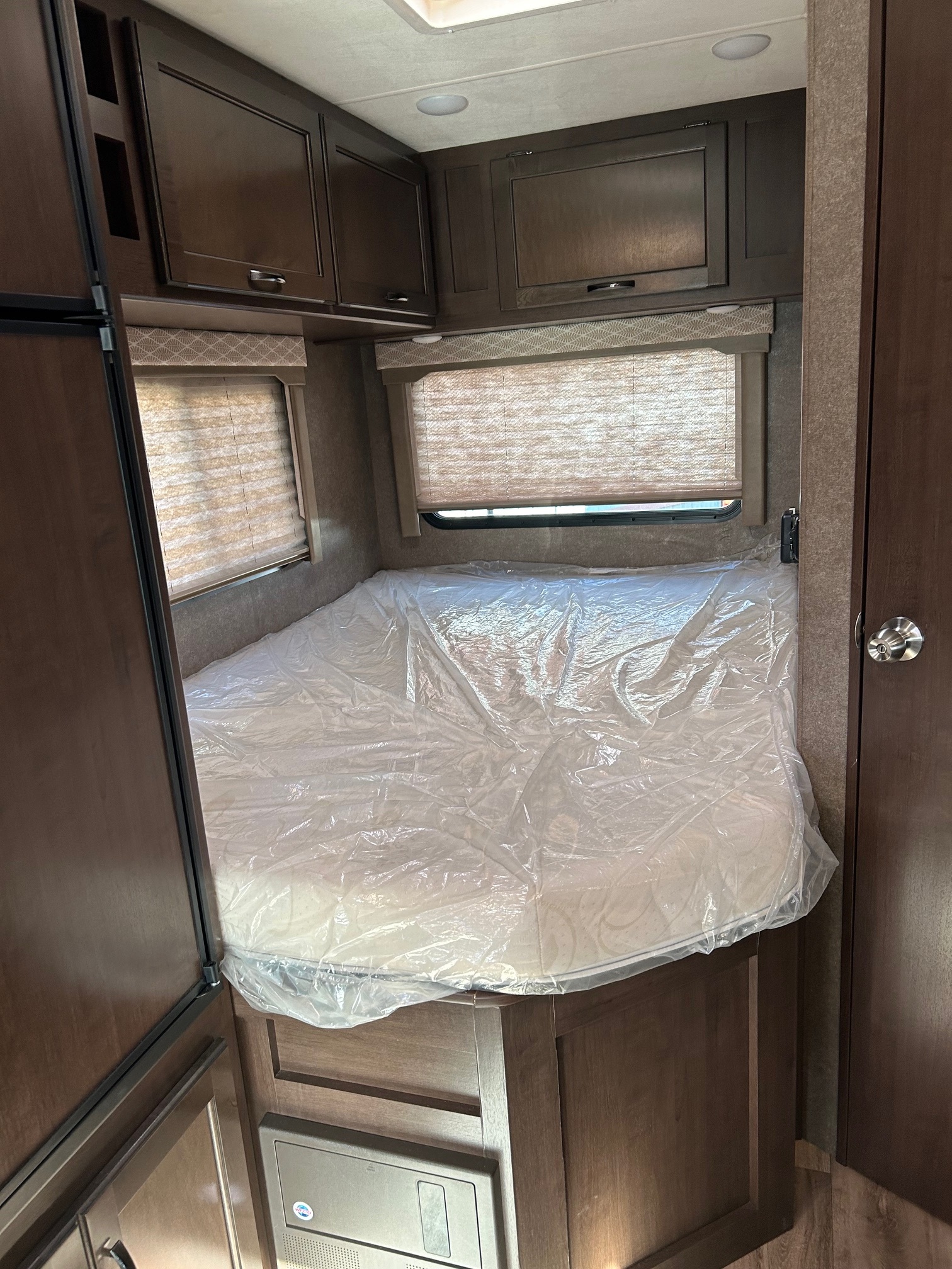 Inside an RV rental: cozy bedroom featuring a new mattress in plastic, overhead storage, and shaded windows. Ready for adventure.. Thor Freedom Elite 22HE 2020