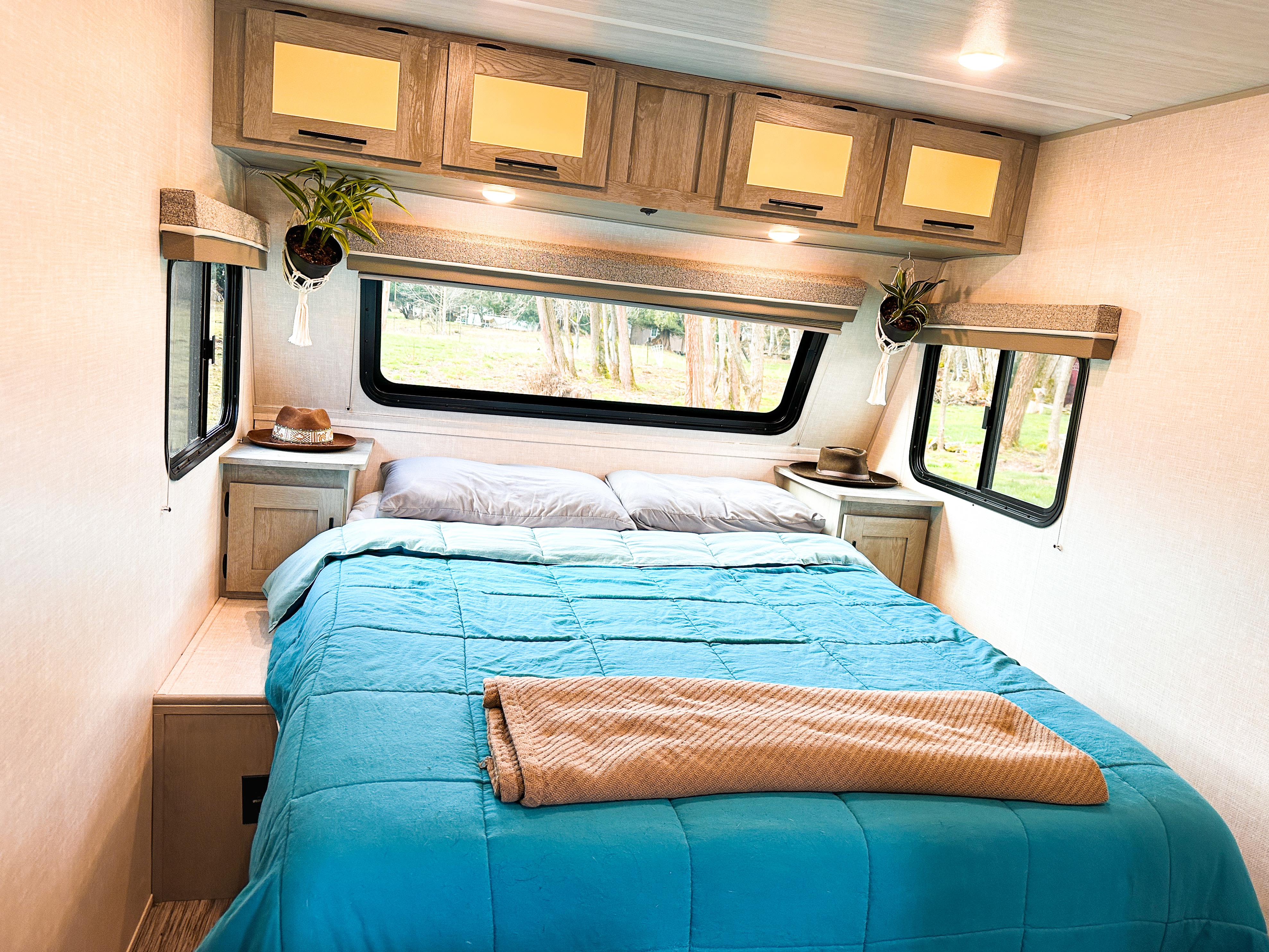 Cozy RV rental bedroom with a comfy blue bed, smart storage, and large windows bringing nature in.. Forest River Ibex 2021